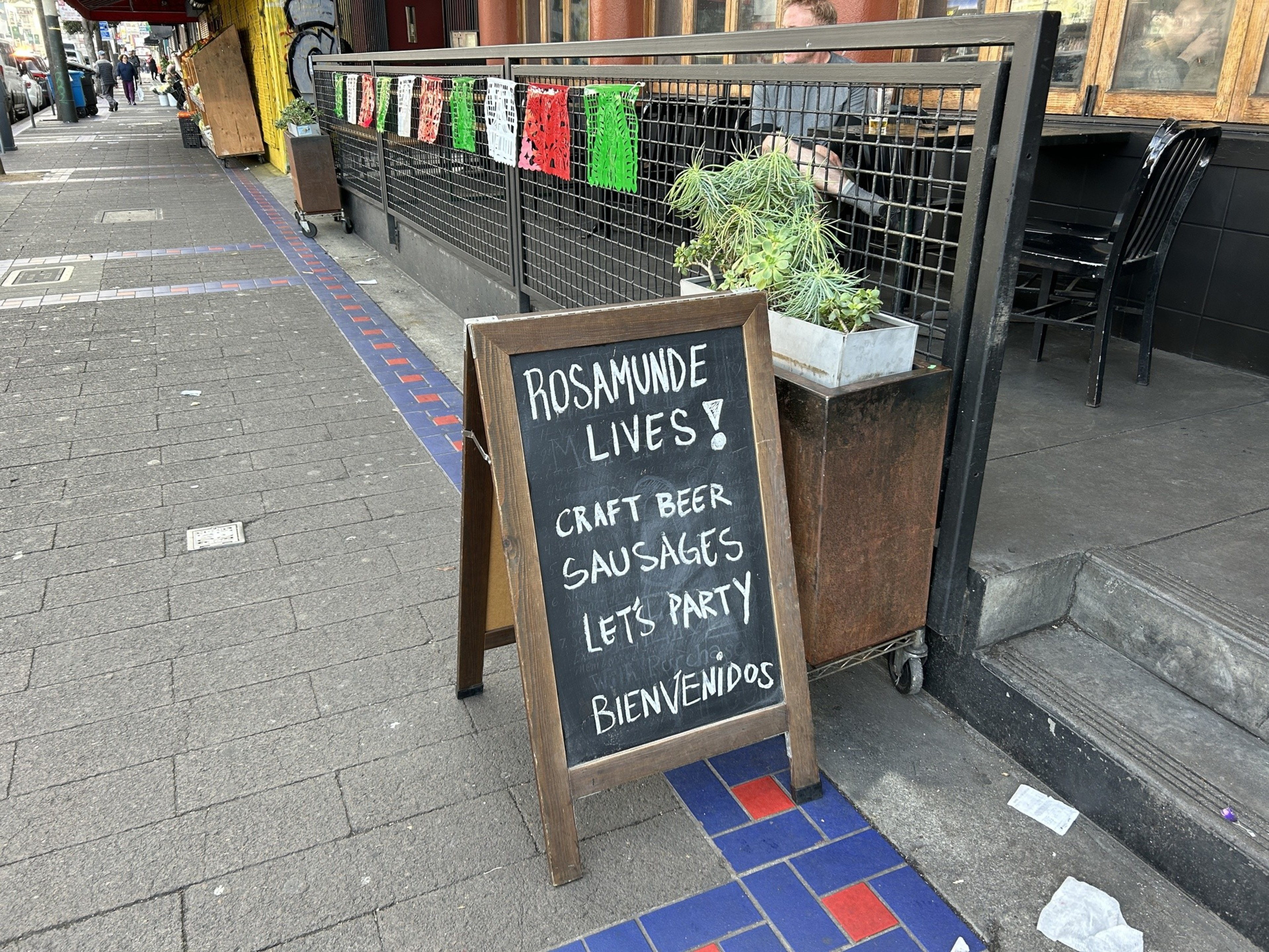 A sandwich board on a sidewalk next to an outdoor restaurant patio announces it's back in business.