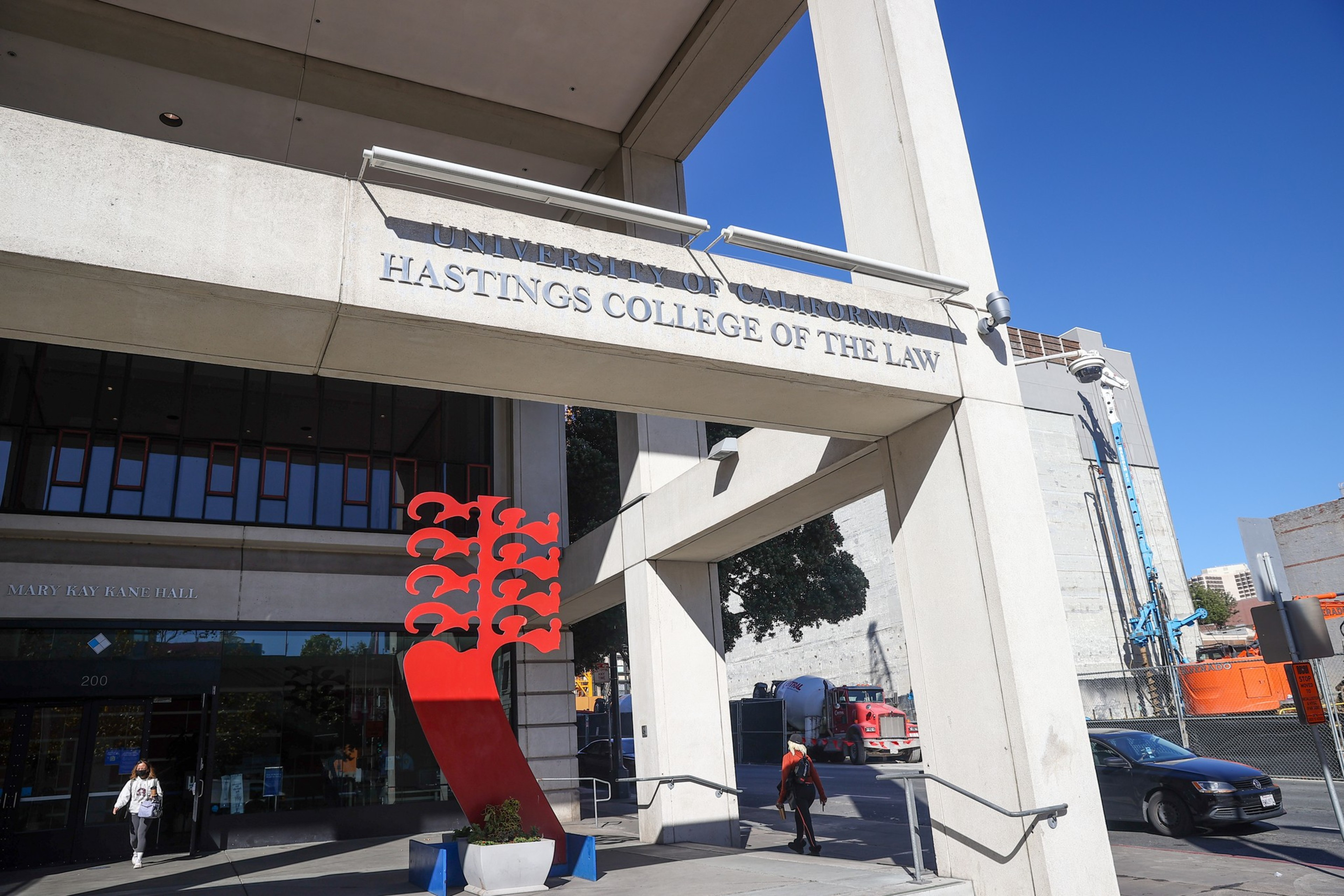 Concrete archway entrance to a law college with a red abstract sculpture on the left. People are walking by under a clear sky.