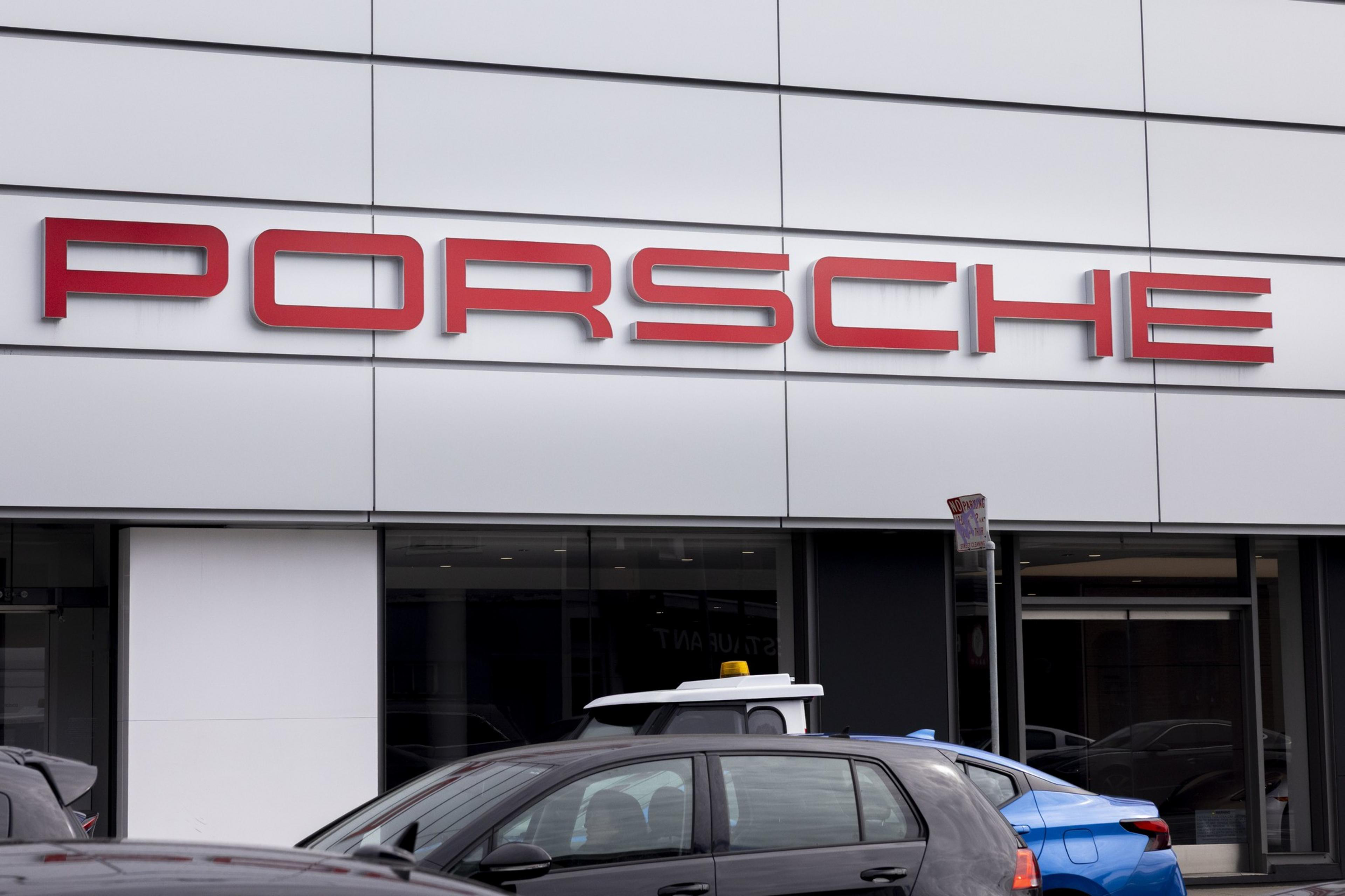 The image shows the facade of a dealership with the word &quot;Porsche&quot; in large red letters. Several cars are parked in the foreground.