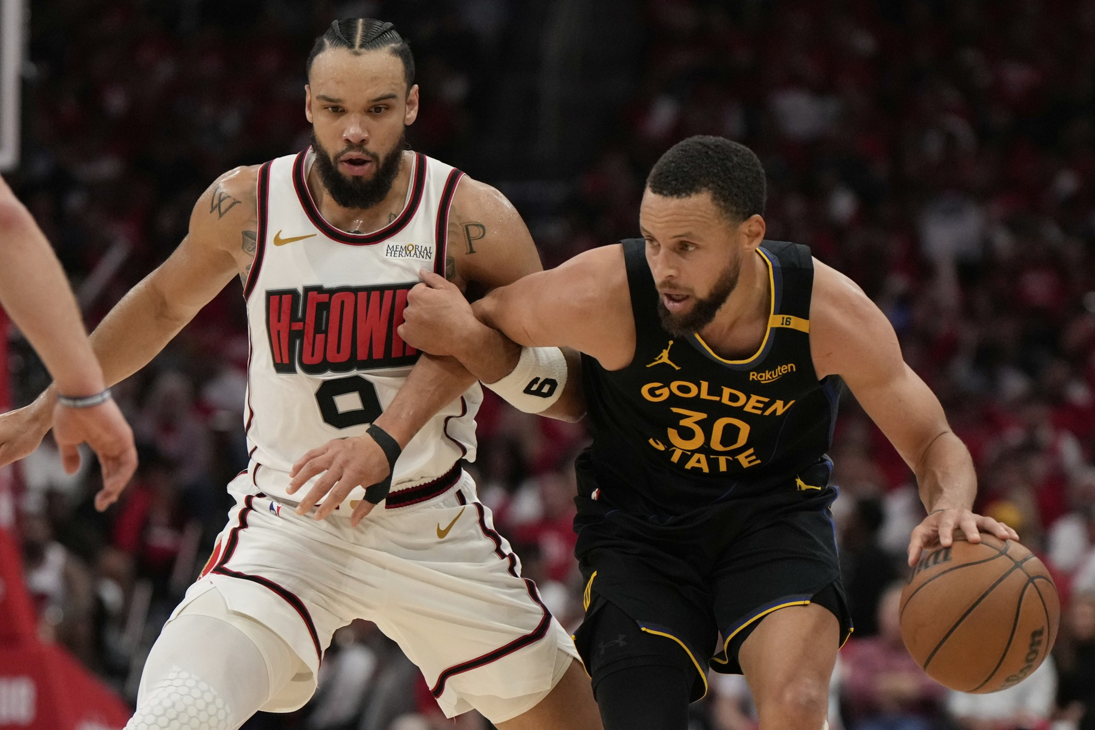 Two basketball players, one in a black Golden State uniform dribbling the ball, and the other in a white H-Town jersey closely defending him.