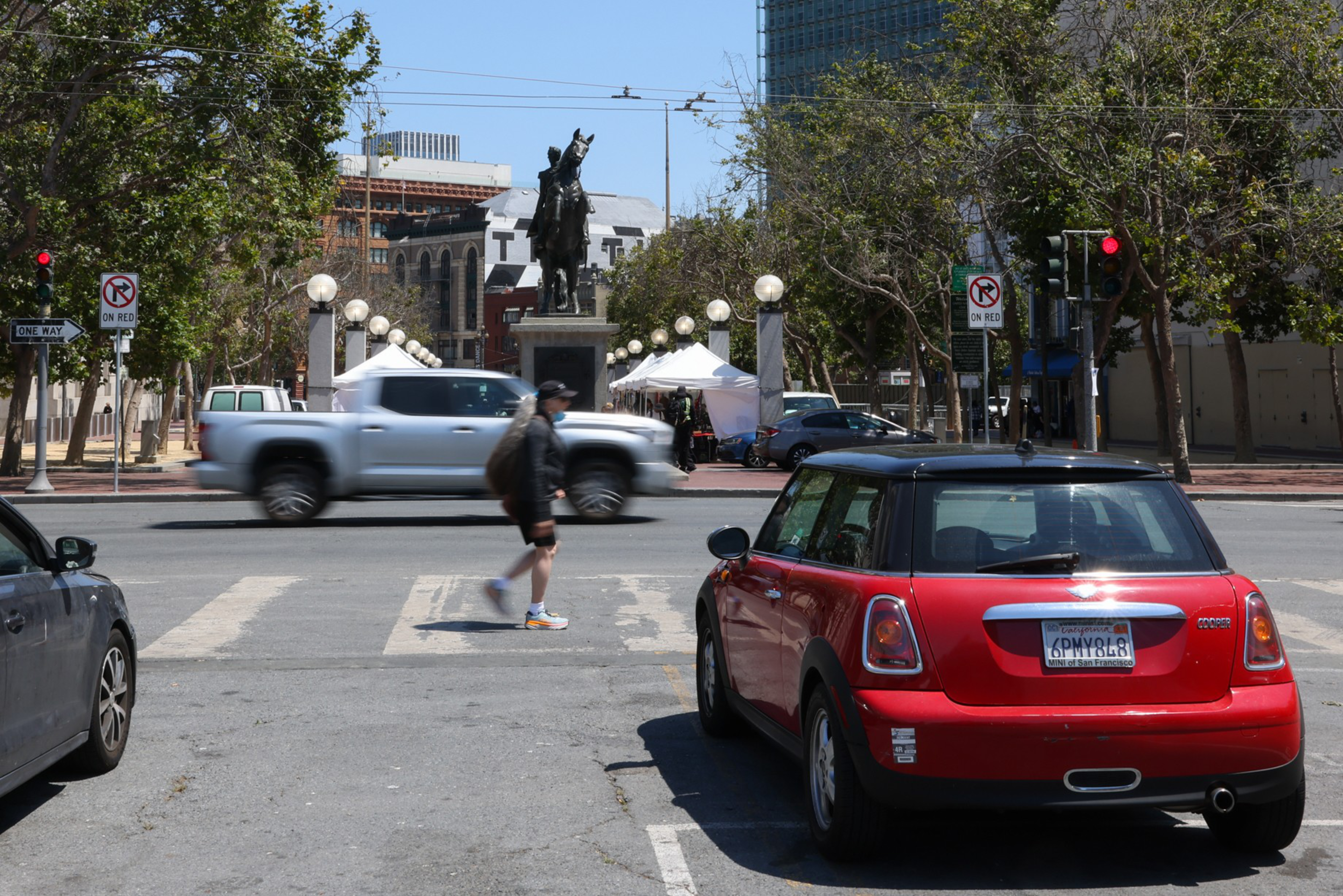 Cars wait at a red light as a pedestrian and a truck drive past an intersection.