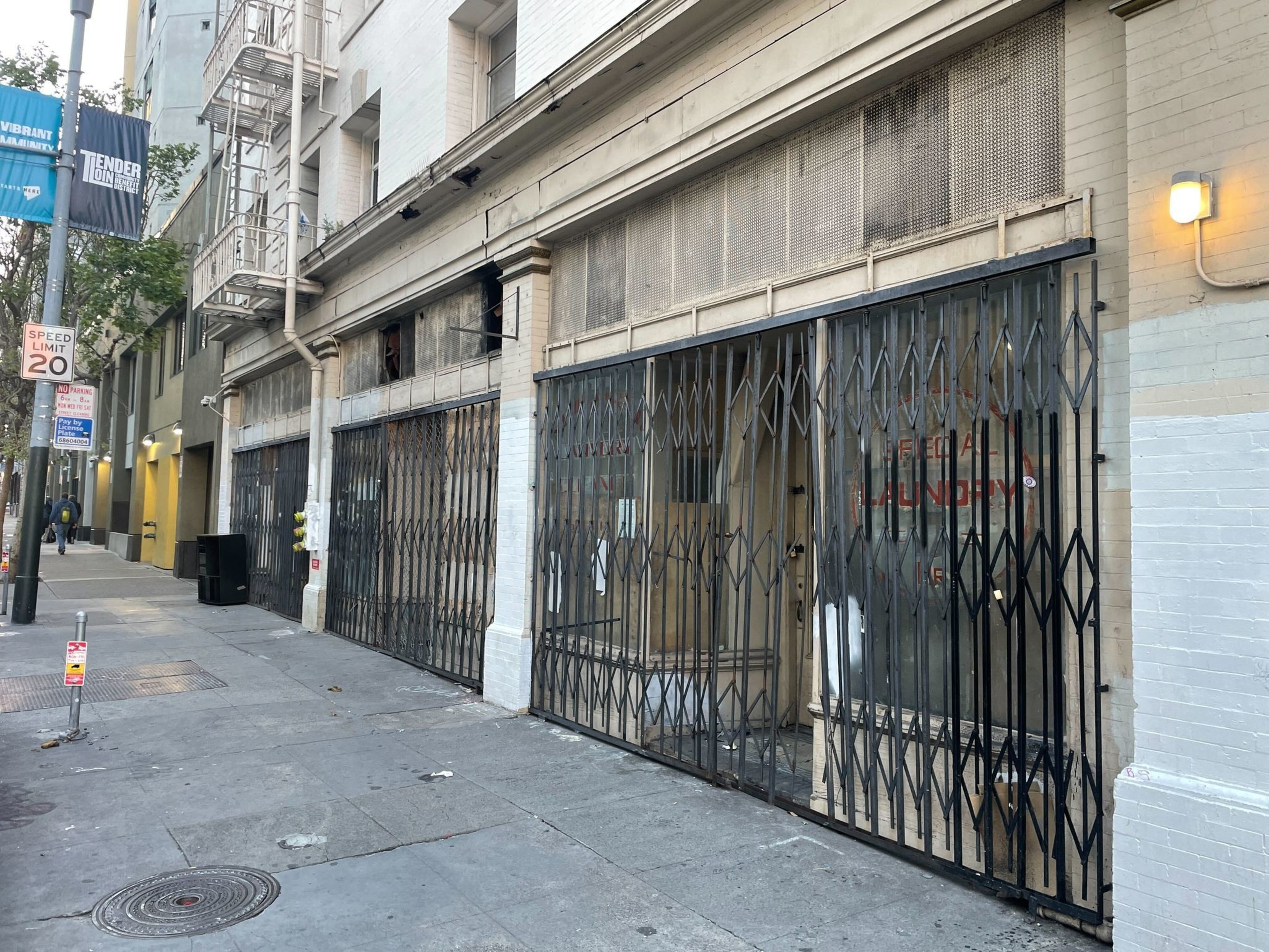A city street with closed shops behind metal security gates, signs of urban life.