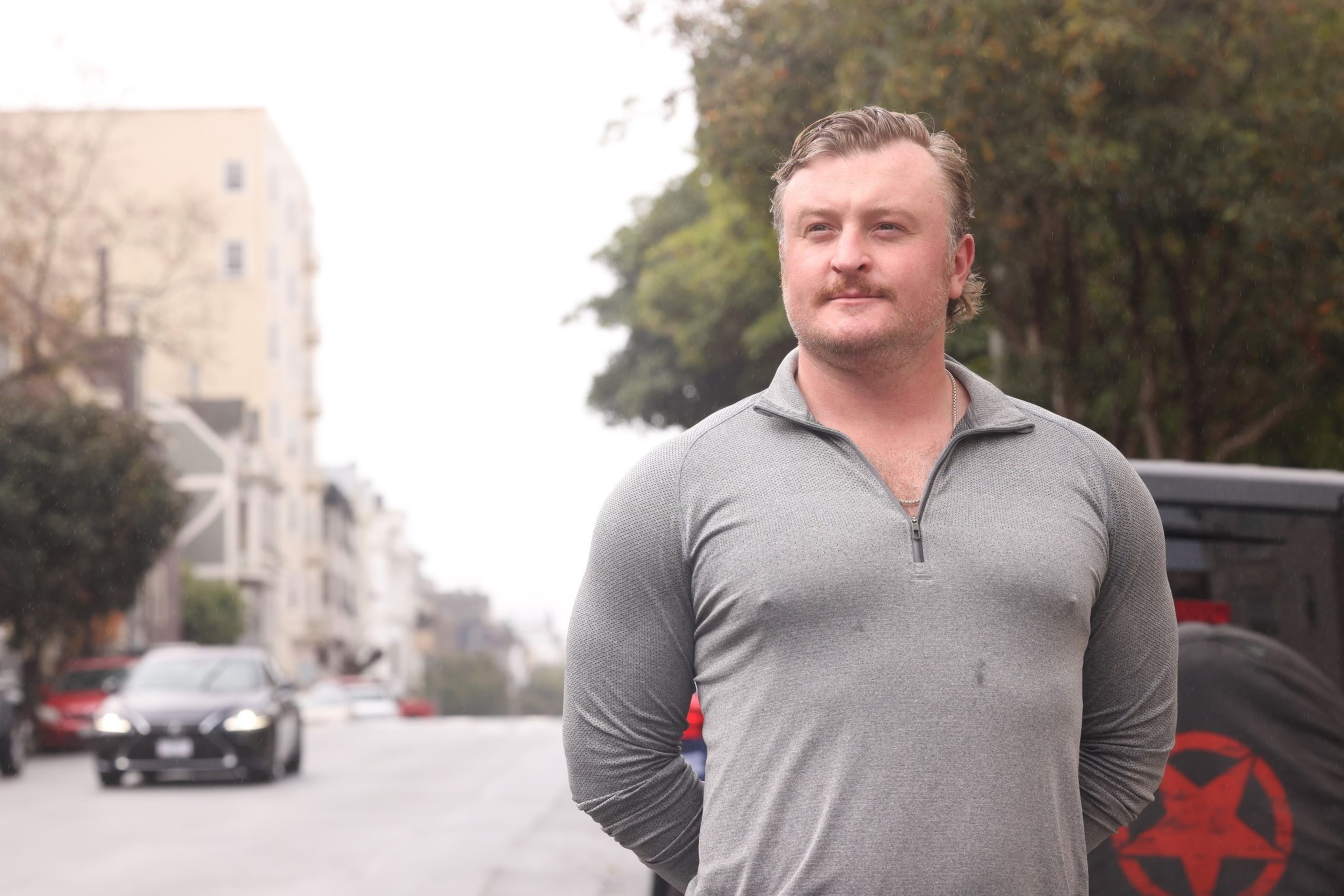A man stands for a portrait on a city street with cars in the background.