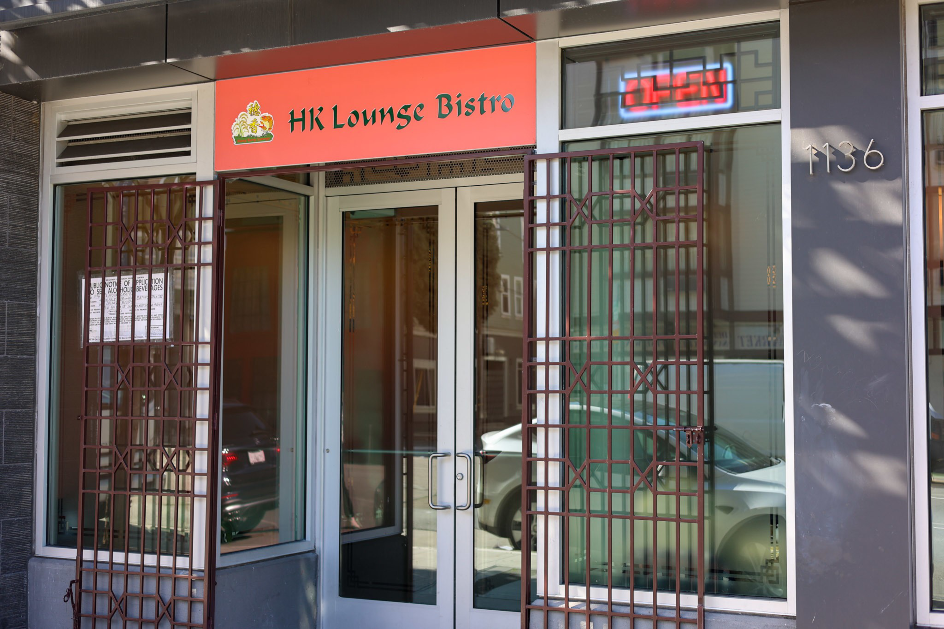 A storefront with double glass doors and barred windows displays a red sign reading "HK Lounge Bistro" above the entrance at number 1136.