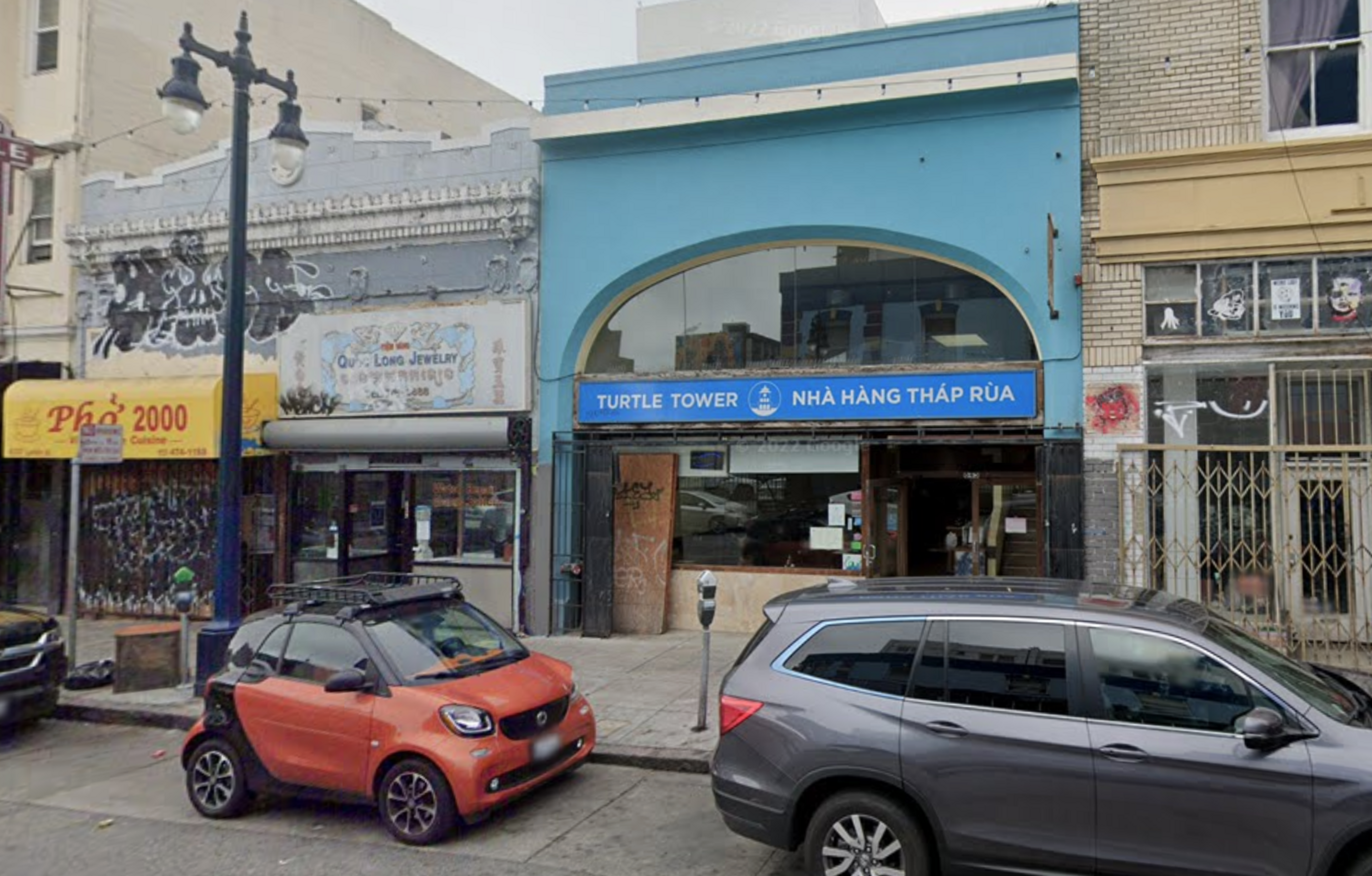 a restaurant on a city street shows two parked cars in front of it.