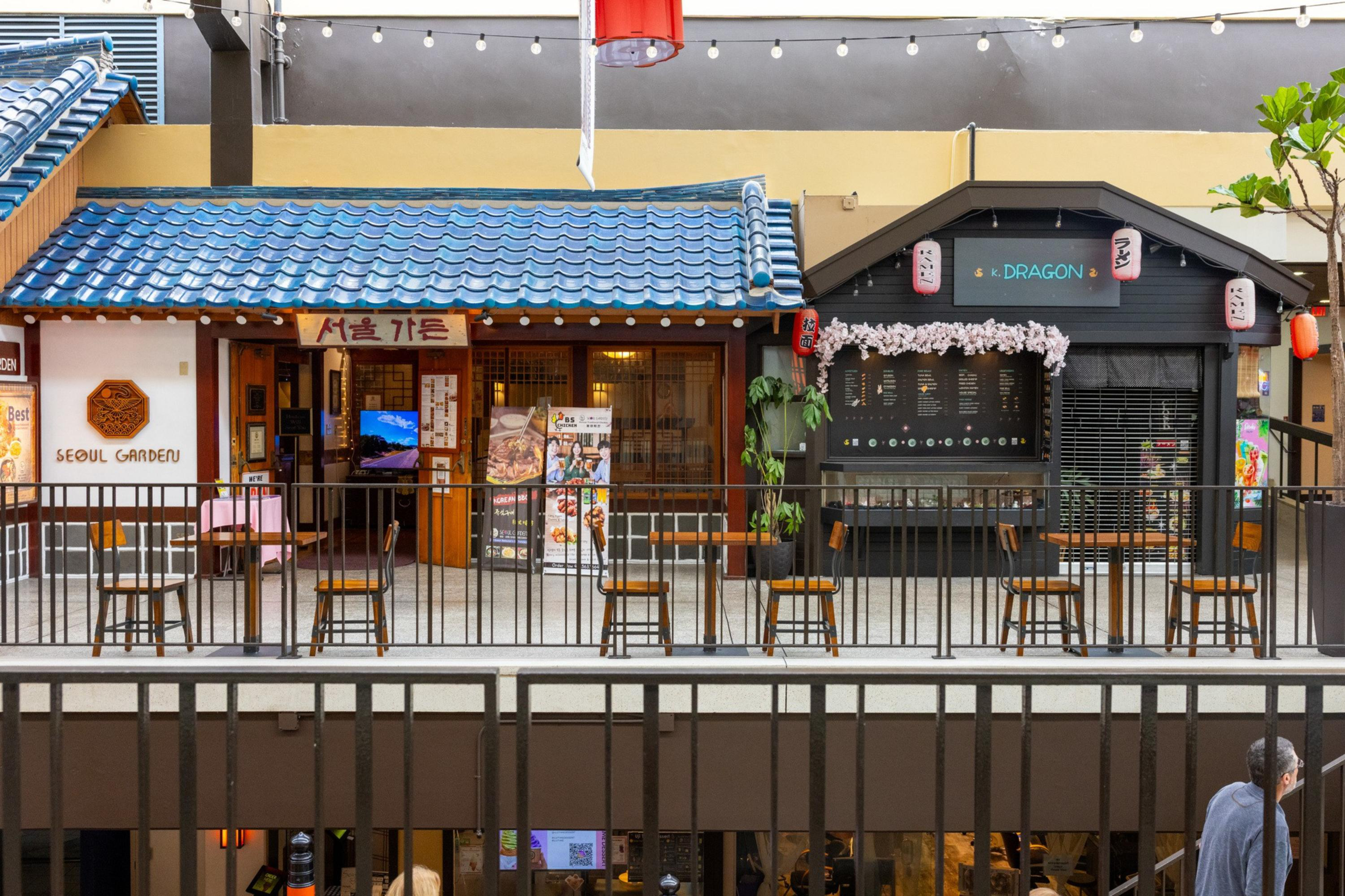 Two adjacent Asian-themed restaurants with outdoor seating are visible, one with a blue tiled roof labeled “Seoul Garden” and the other decorated with lanterns and flowers.