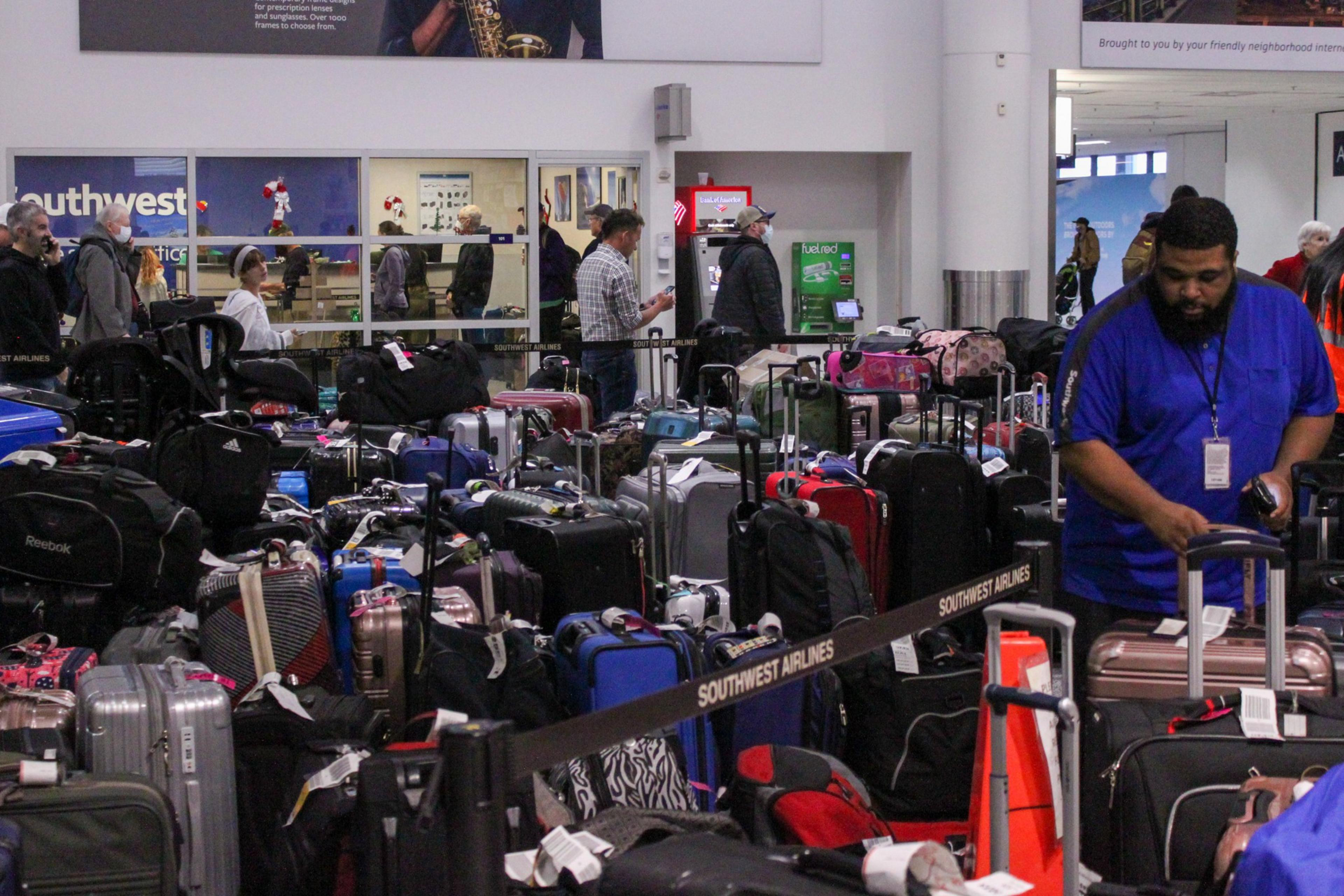 Numerous suitcases and bags are crowded behind a Southwest Airlines barrier in an airport, with several people standing or waiting nearby.