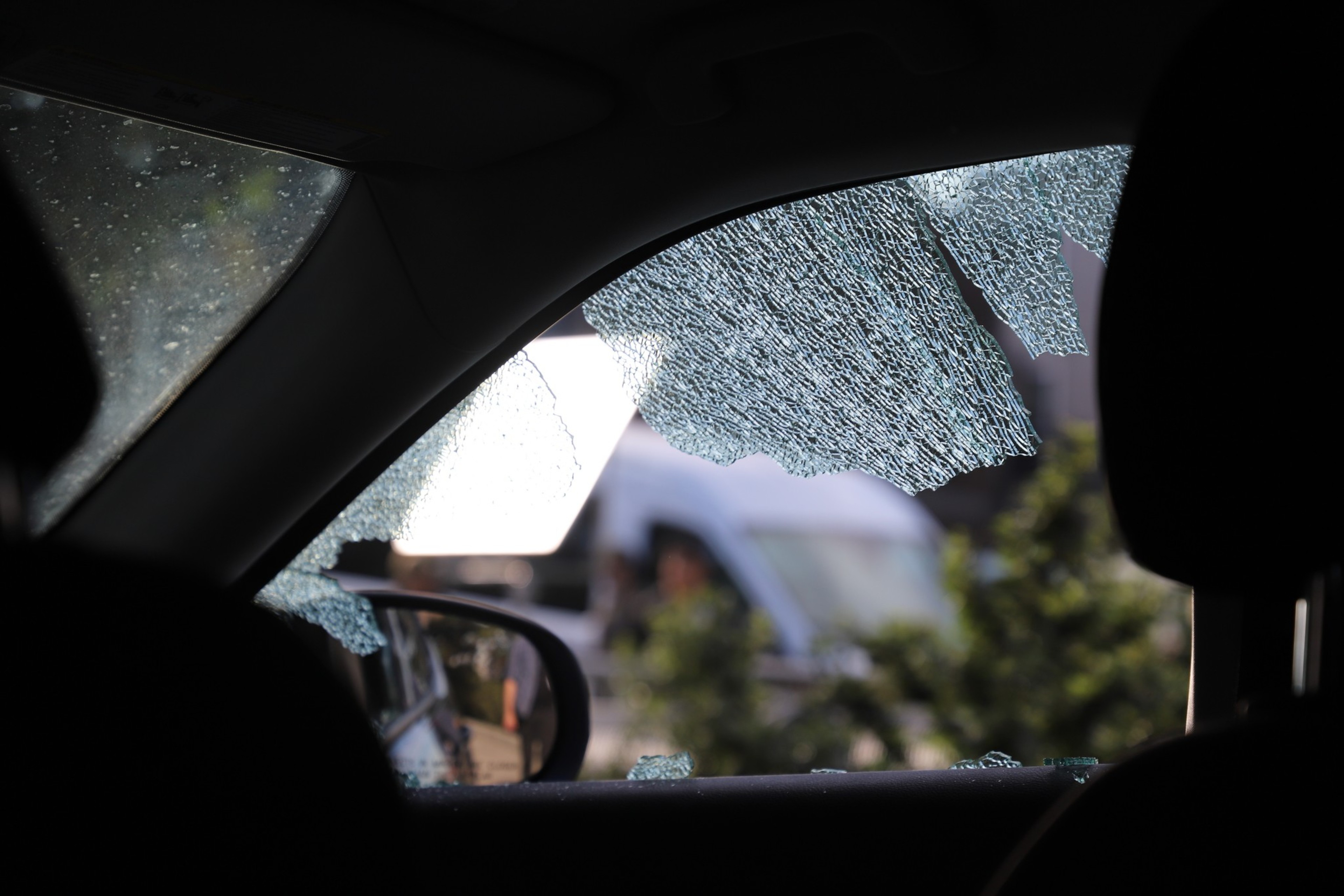 Shattered car window glass with a blurred outdoor background.