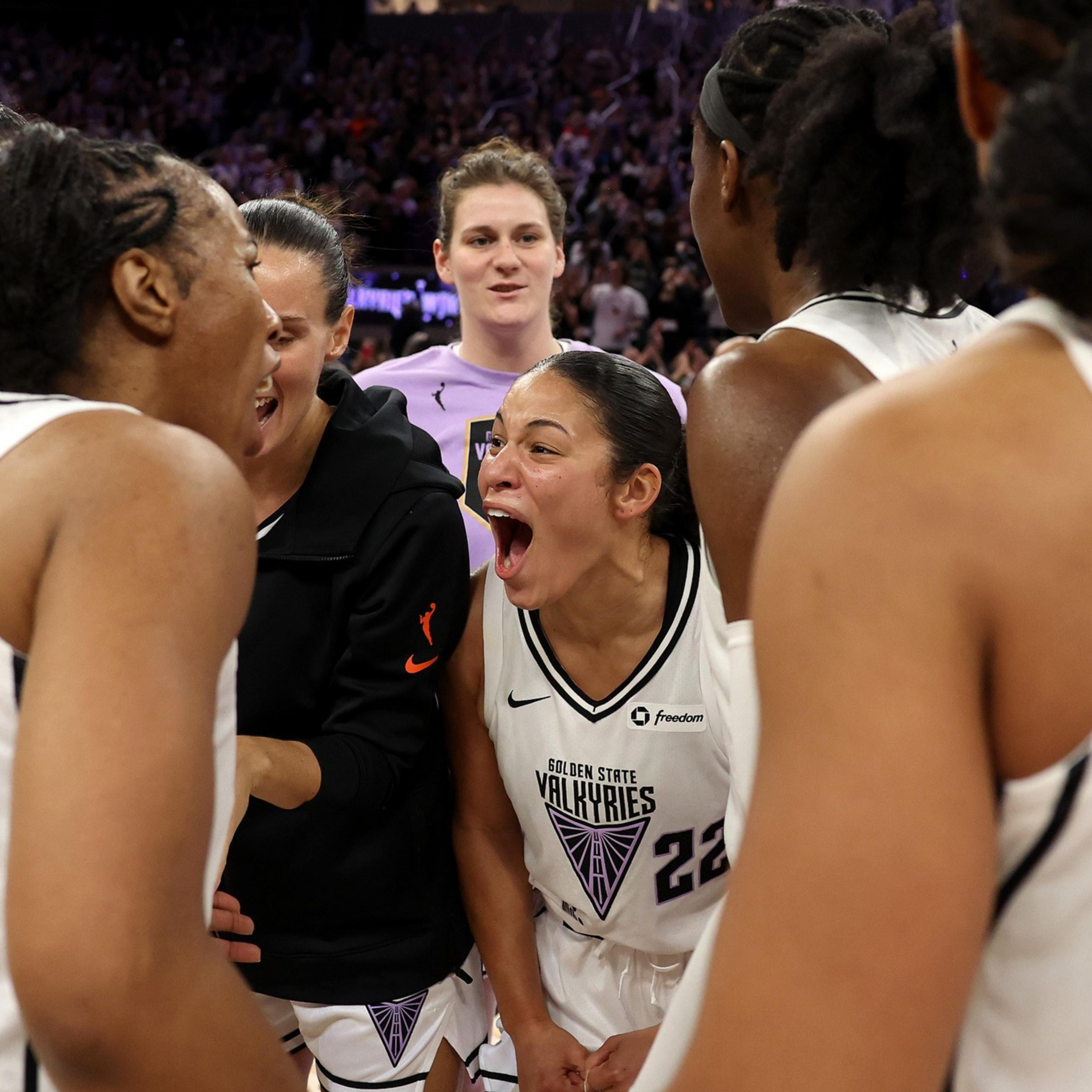 A group of basketball players in white jerseys are huddled together, excitedly talking and yelling, creating an atmosphere of celebration and teamwork.