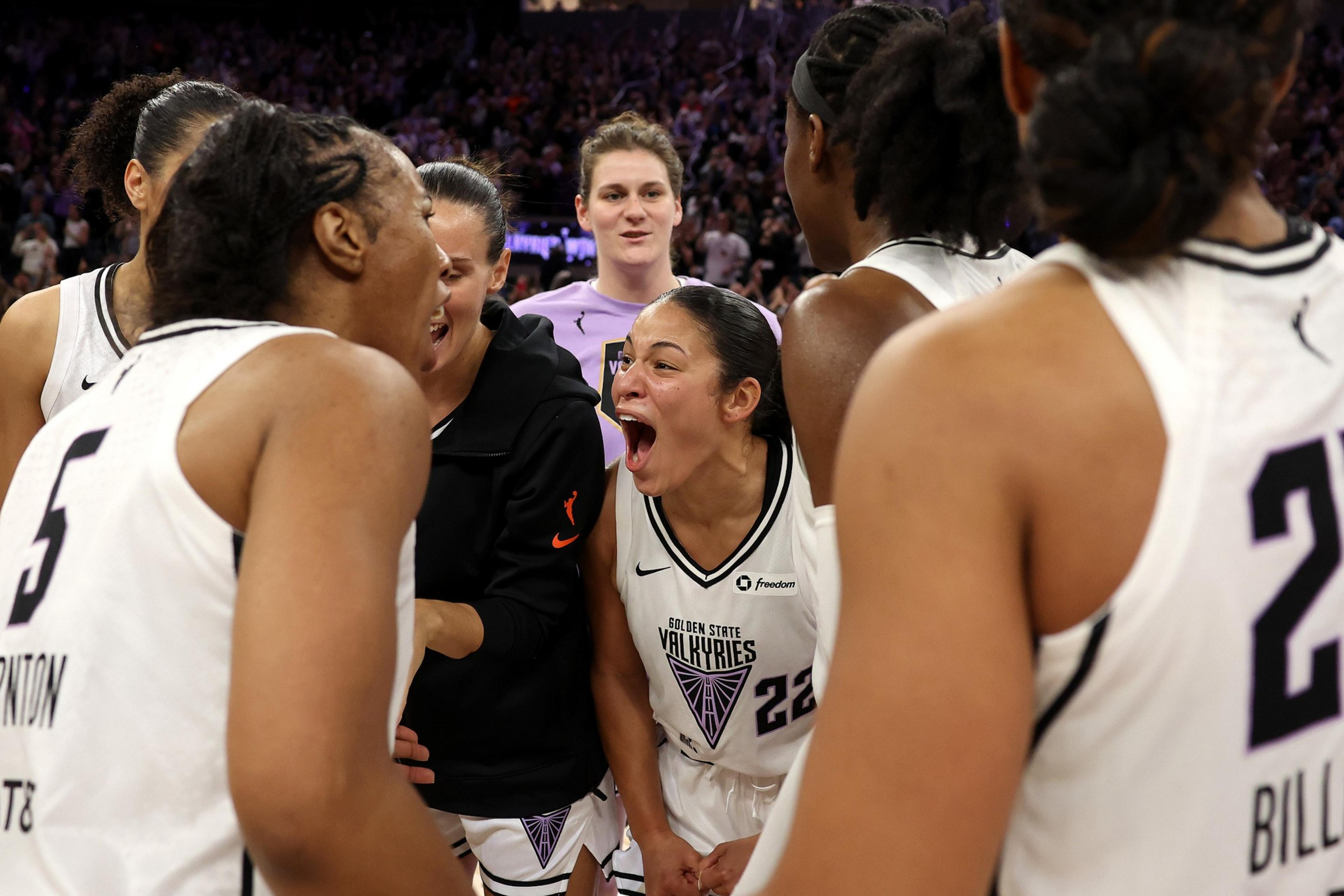 A group of basketball players in white jerseys are huddled together, excitedly talking and yelling, creating an atmosphere of celebration and teamwork.