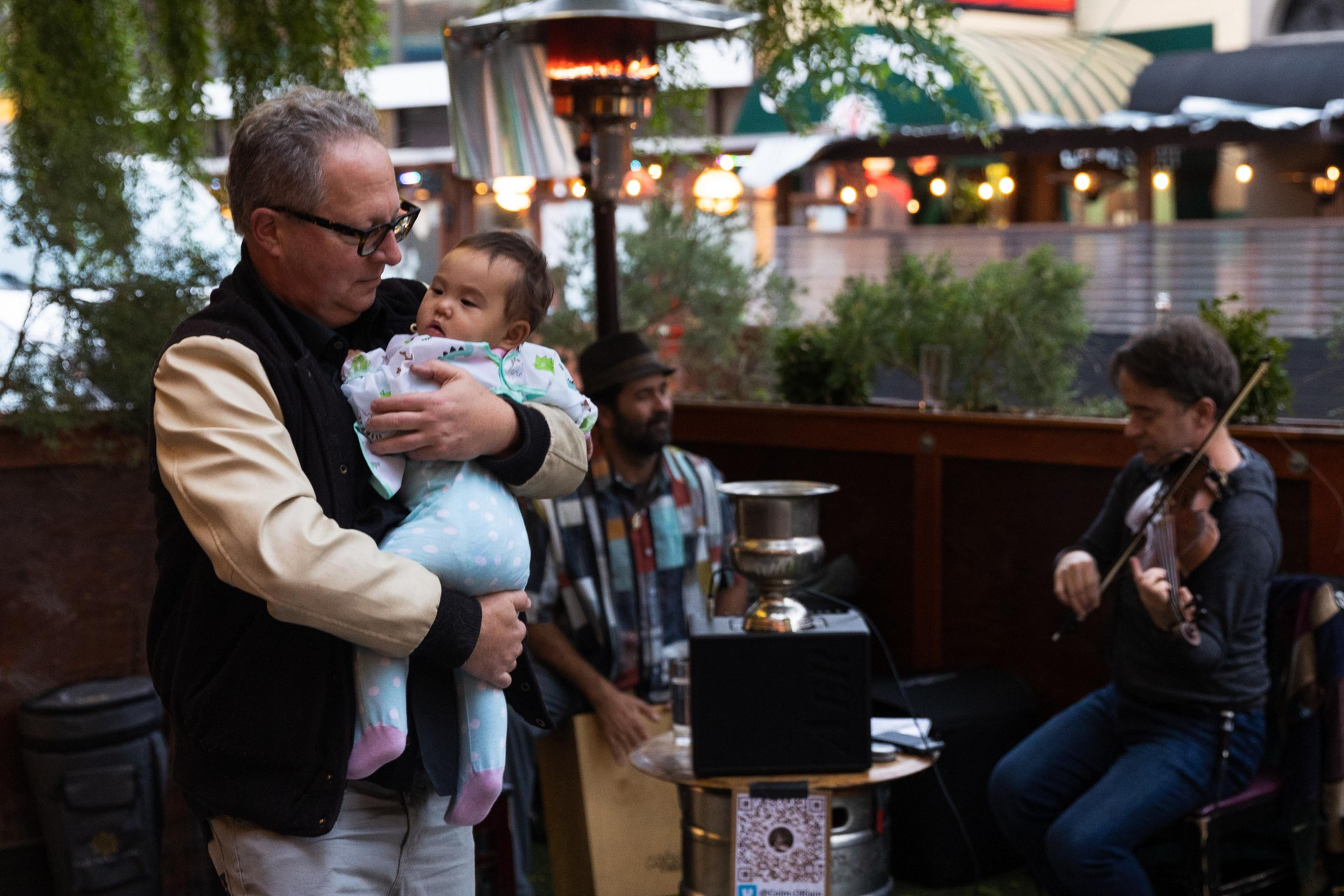 Robert Brownstone dances with Lucy Mae, a friendâ€™s baby, while Colm Oâ€™Riain and Wade Peterson perform in the parklet at Belle Cora in the North Beach neighborhood of San Francisco
