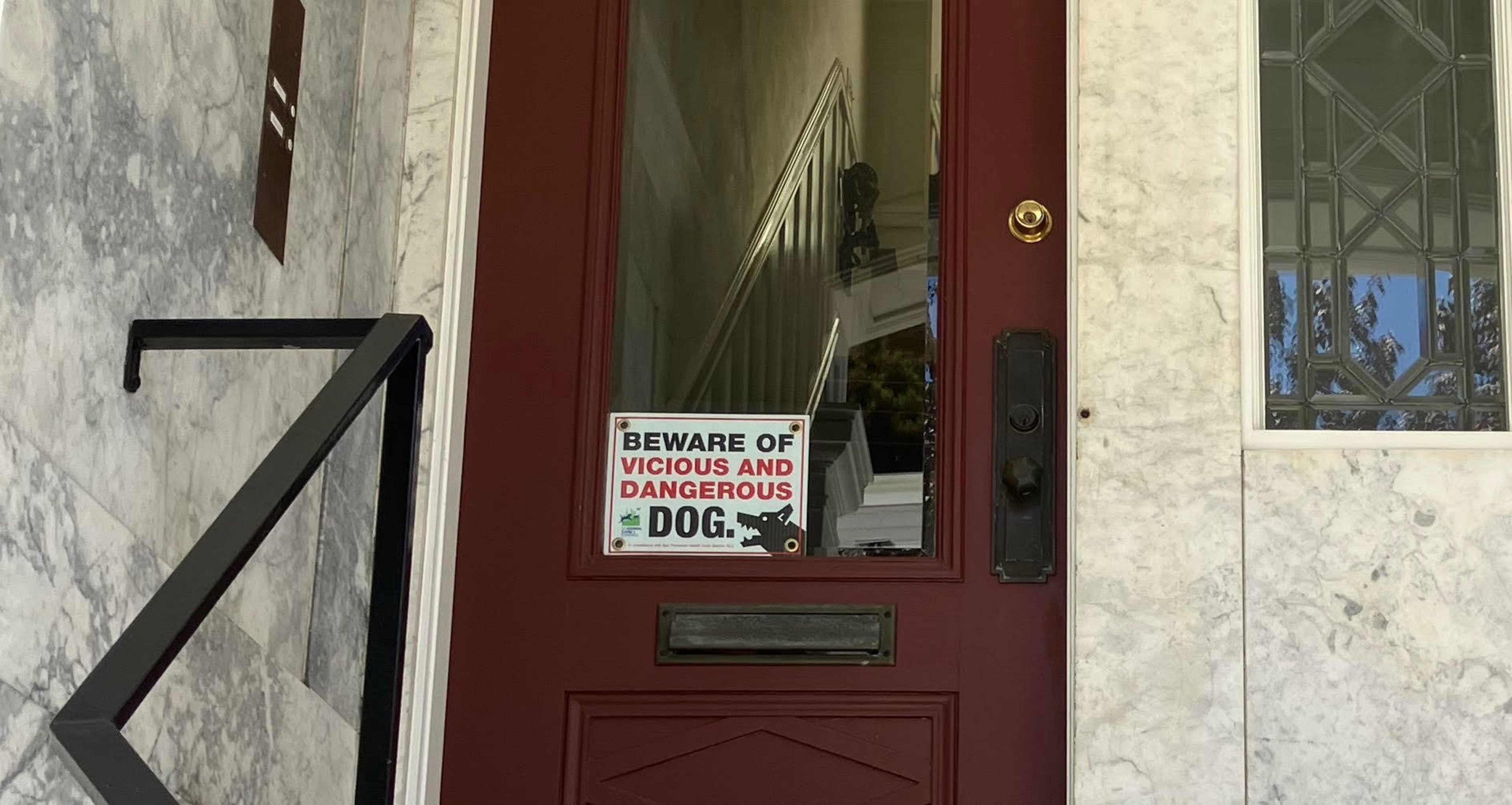 A red door with a glass panel has a sign reading “Beware of vicious and dangerous dog” placed on the lower part of the glass.