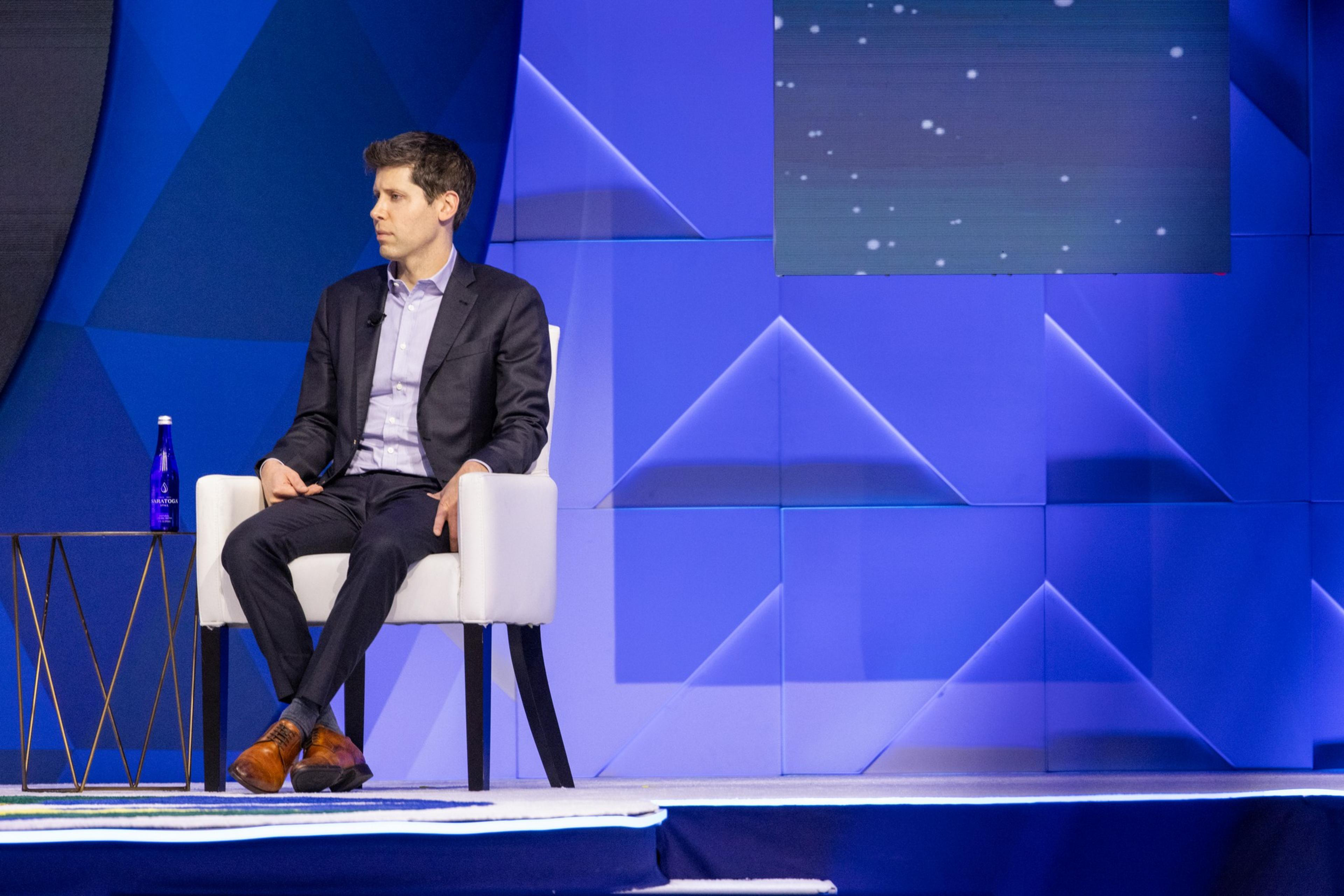 Sam Altman, CEO of OpenAI looks offscreen with a blue background.