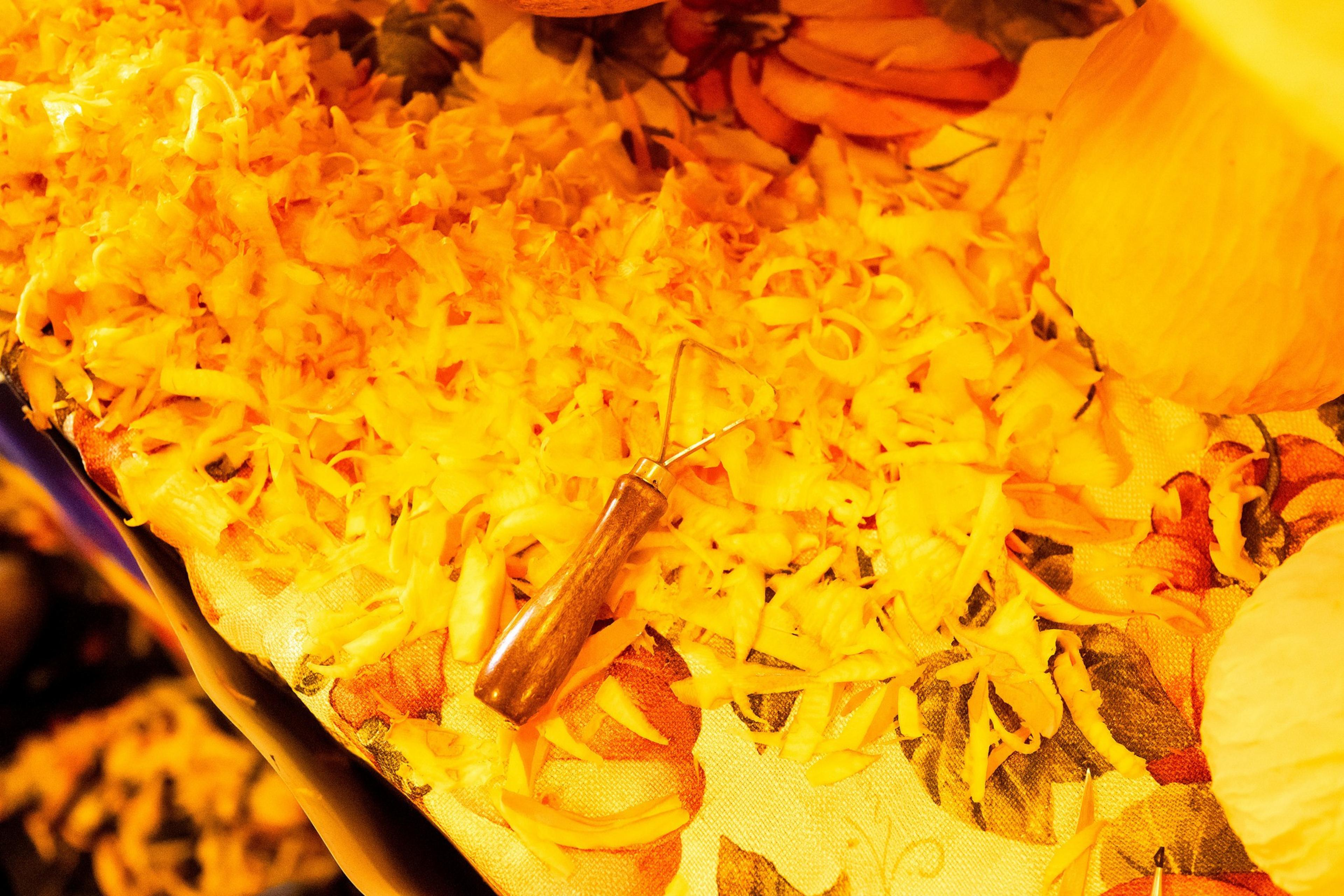 The image shows a carving tool on a table covered with orange pumpkin shavings and floral-patterned fabric, suggesting a pumpkin carving activity.
