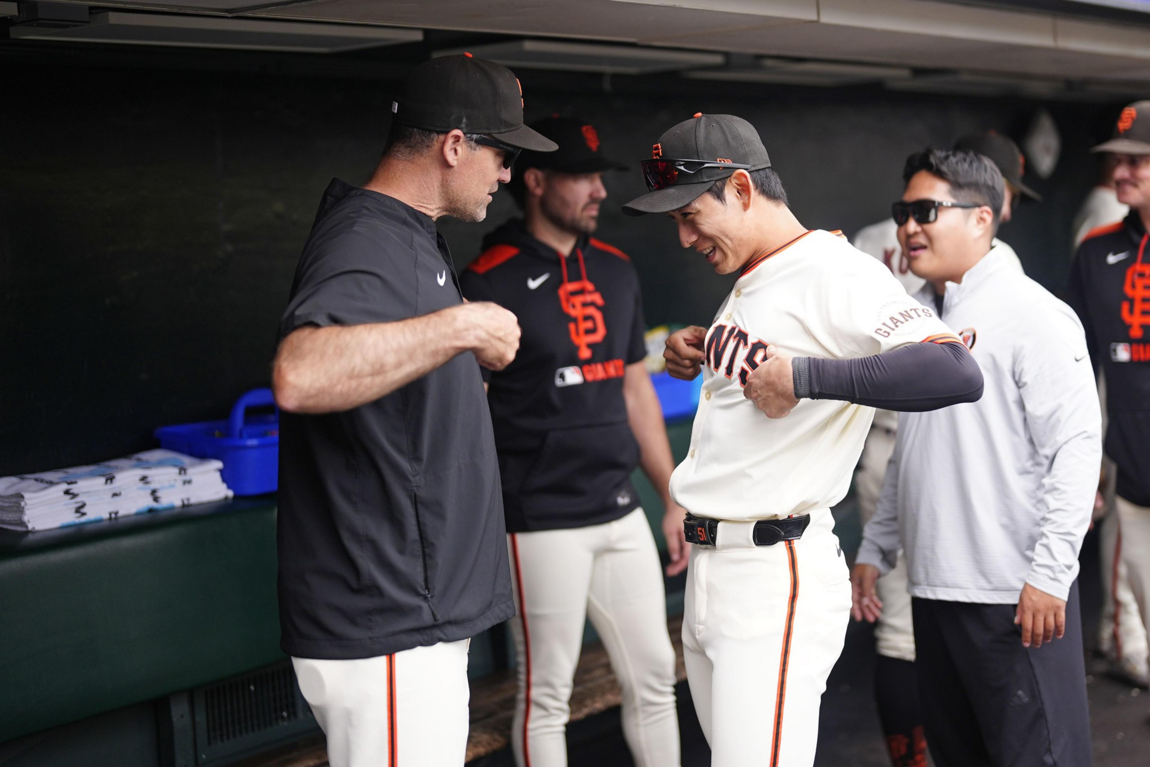 Two baseball players and two staff members in San Francisco Giants gear share a light moment in the dugout before a game.