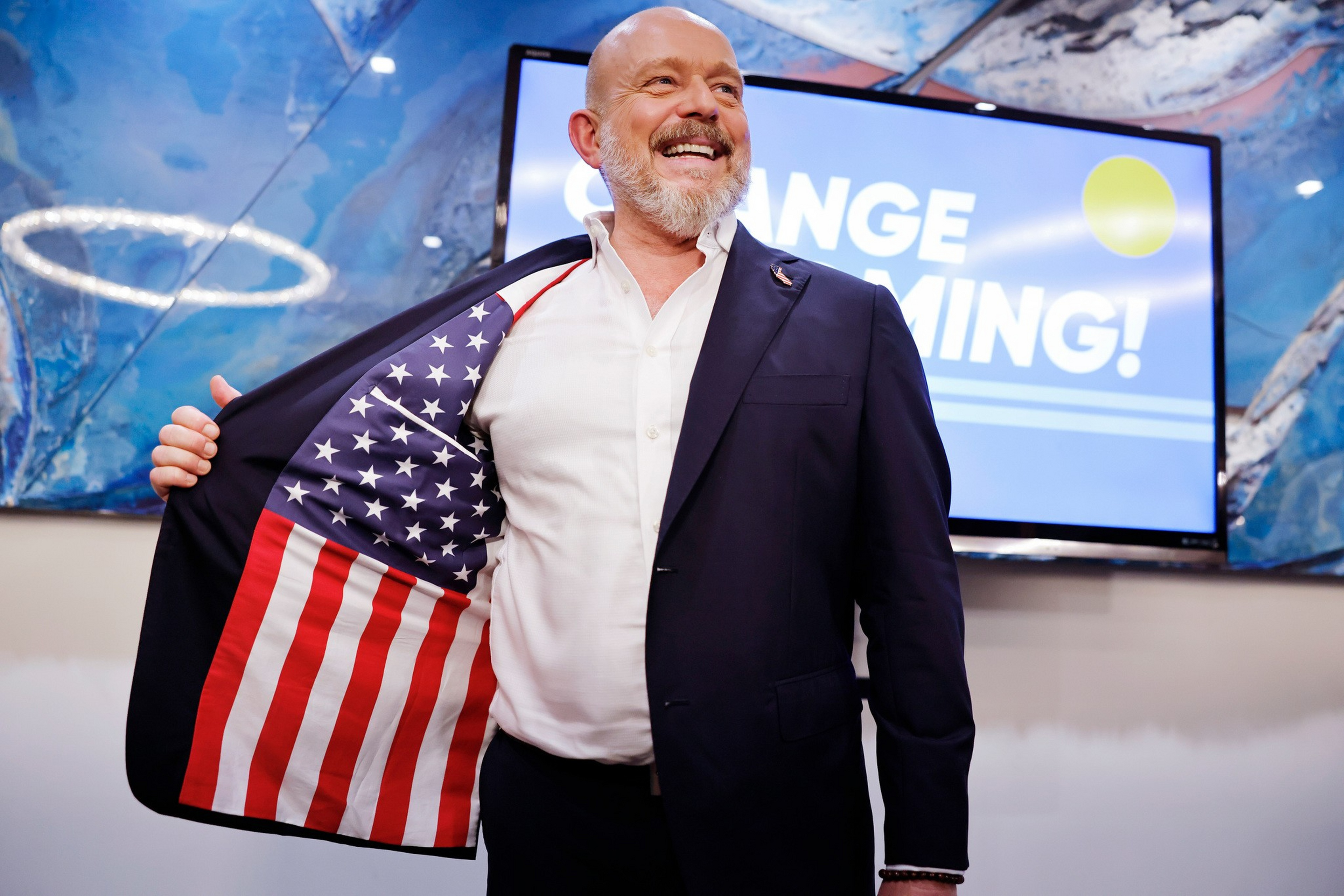 A smiling man in a dark suit shows the inside lining of his jacket, which features the American flag.