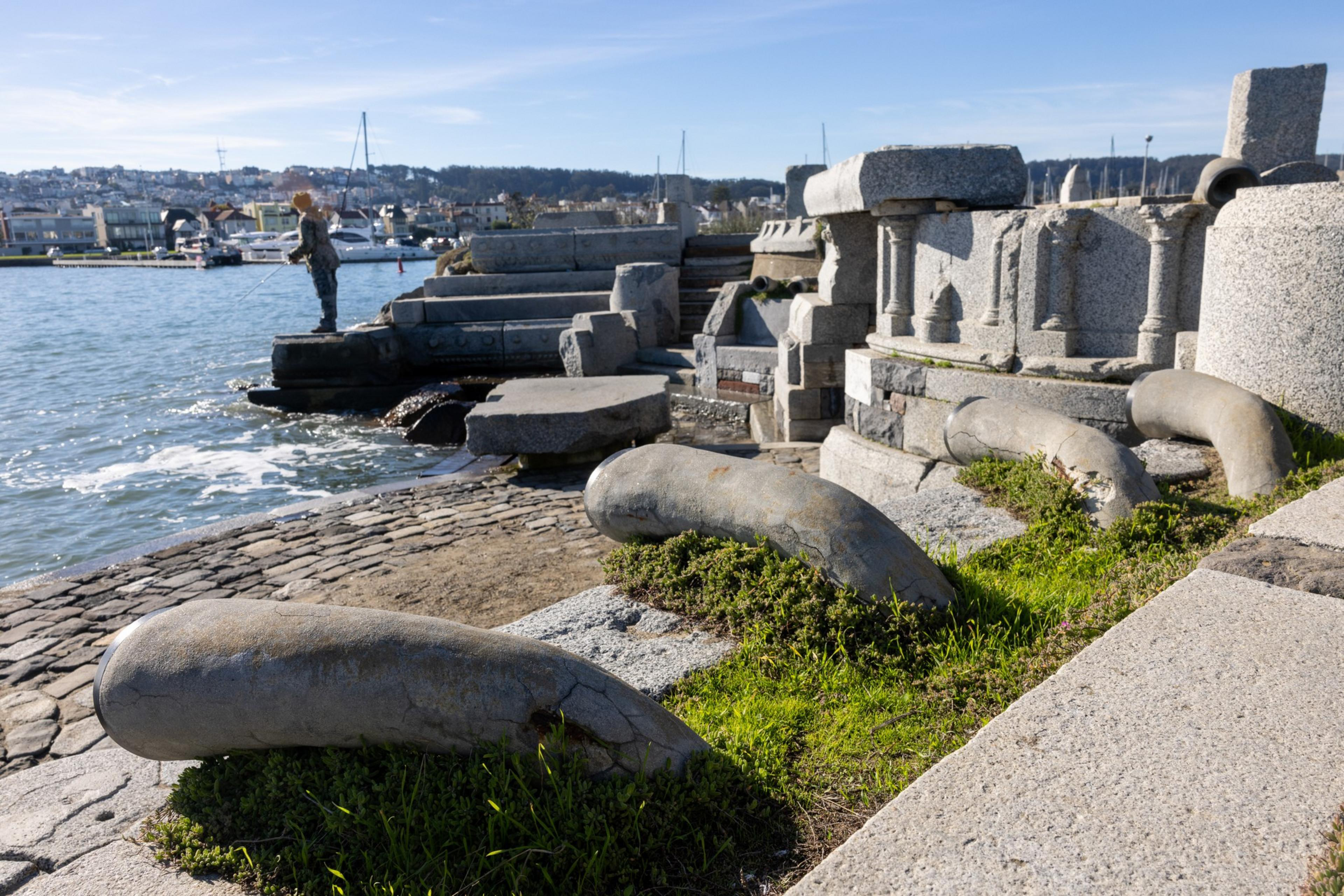 A person fishes off a jetty with stone and cement sculpture around them.