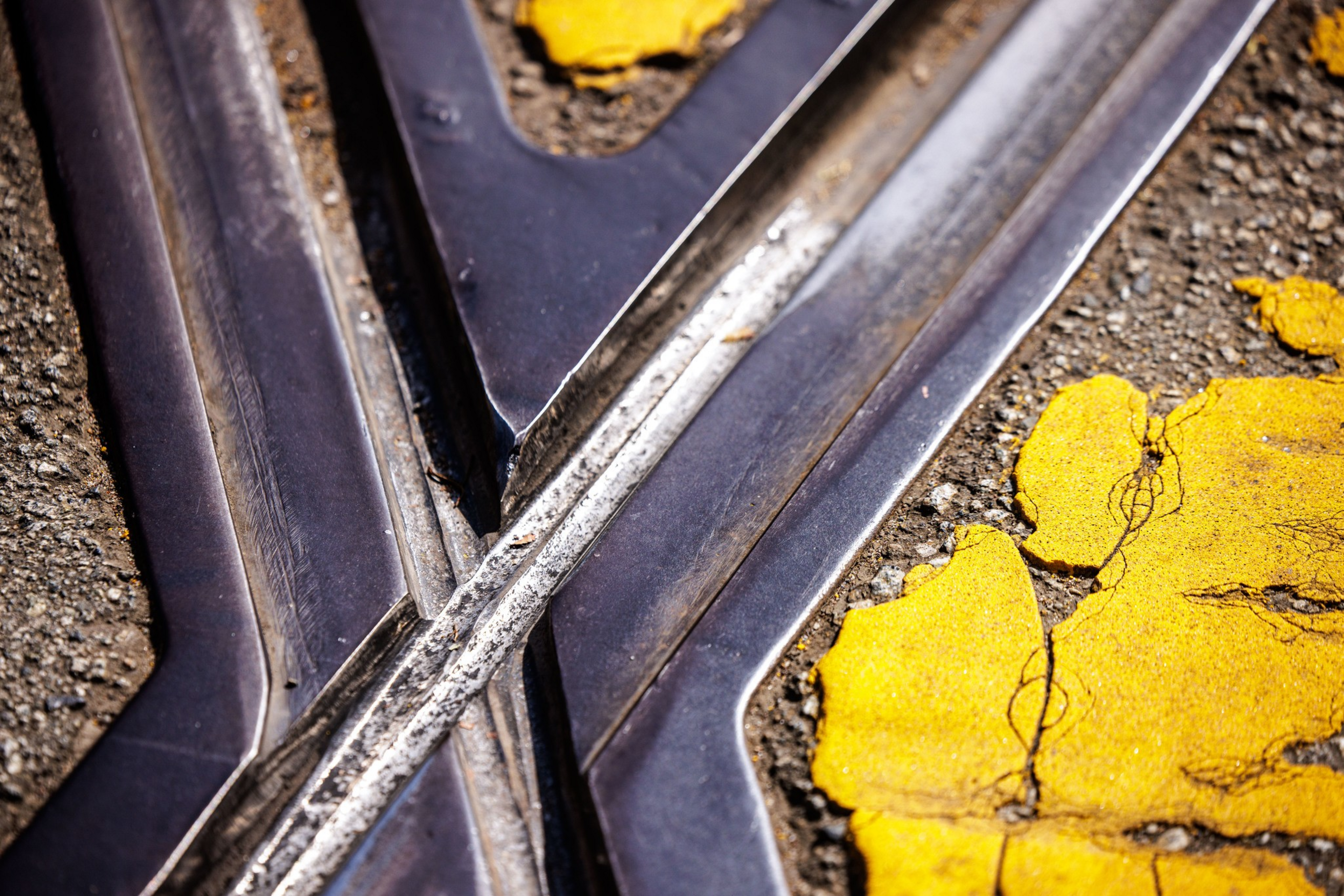 Close-up of intersecting metal railroad tracks with worn, cracked yellow paint on the surrounding textured asphalt.
