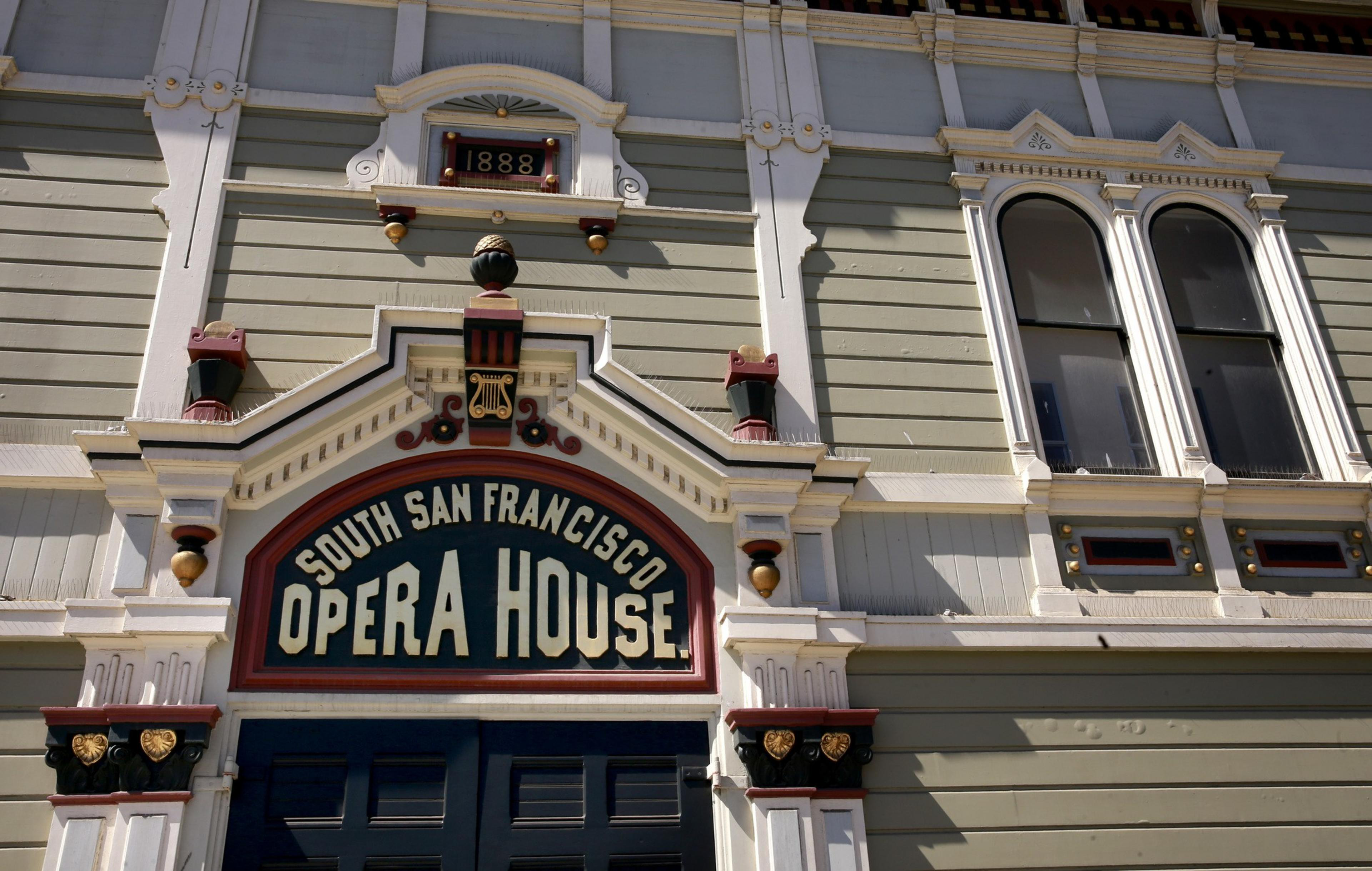 The image shows the facade of the South San Francisco Opera House, with ornate detailing and a sign reading &quot;1888&quot; above the entrance.