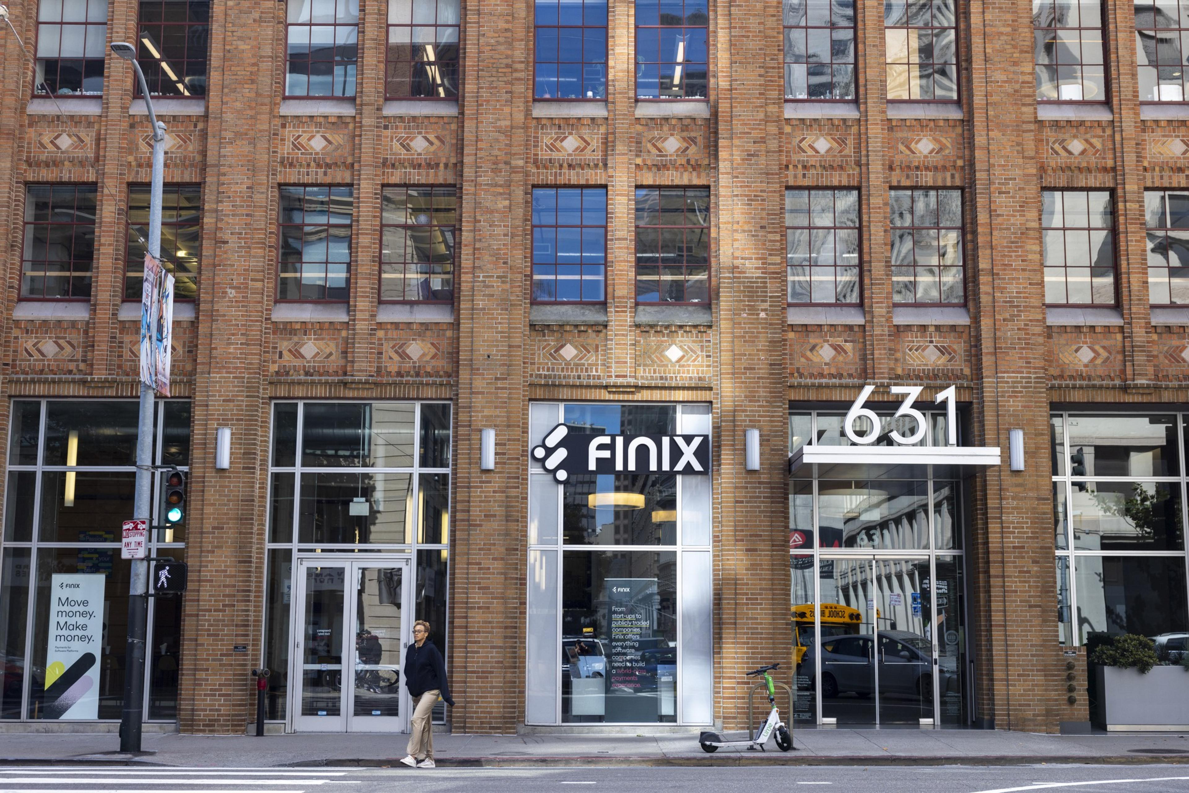 A modern brick building with large windows houses Finix at 631. A person walks by, and an electric scooter is parked nearby. A sign reads, &quot;Move money. Make money.&quot;