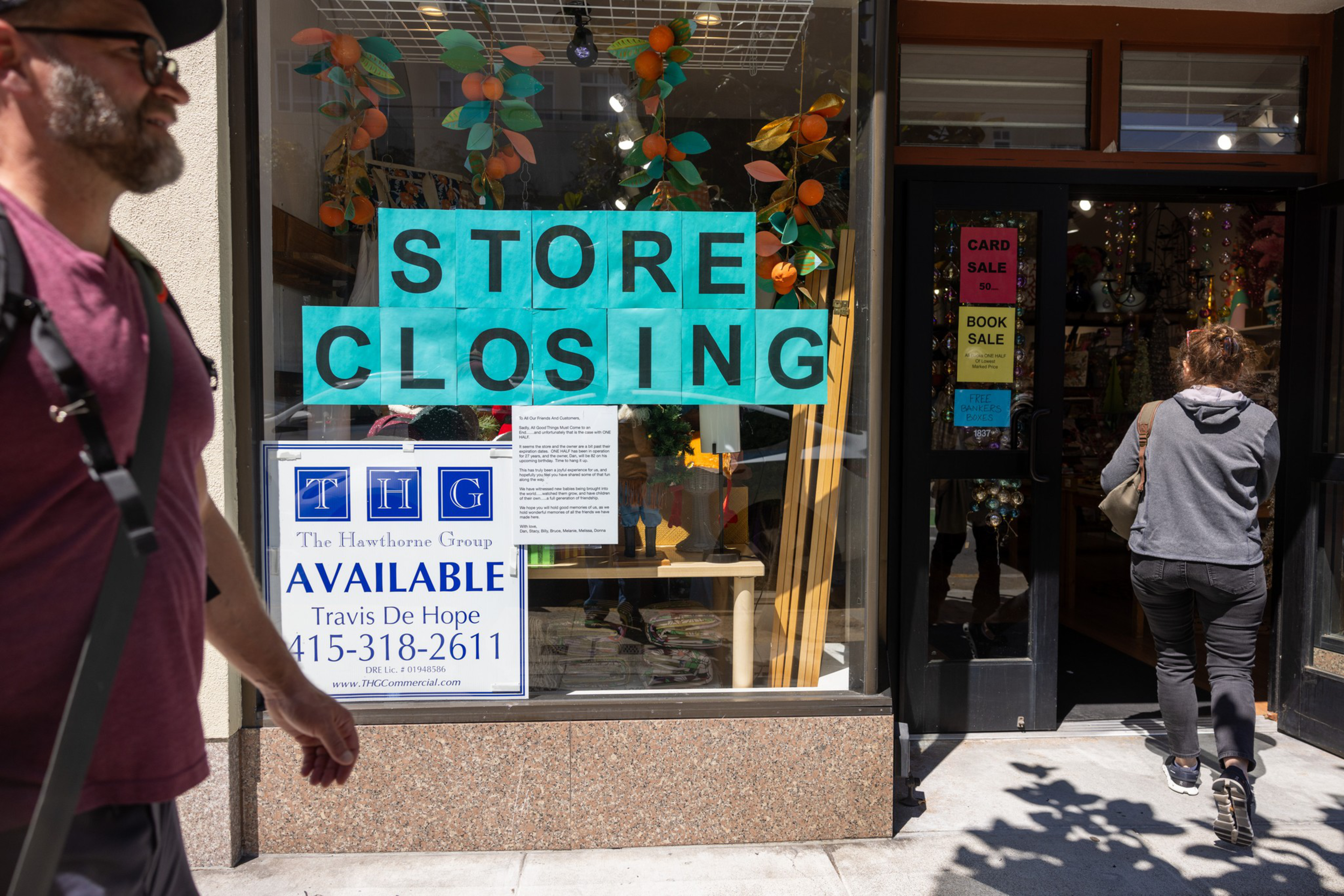 A storefront with signs reading "STORE CLOSING" and "AVAILABLE" with contact details. One person walks past, while another enters. Decorations are visible inside.