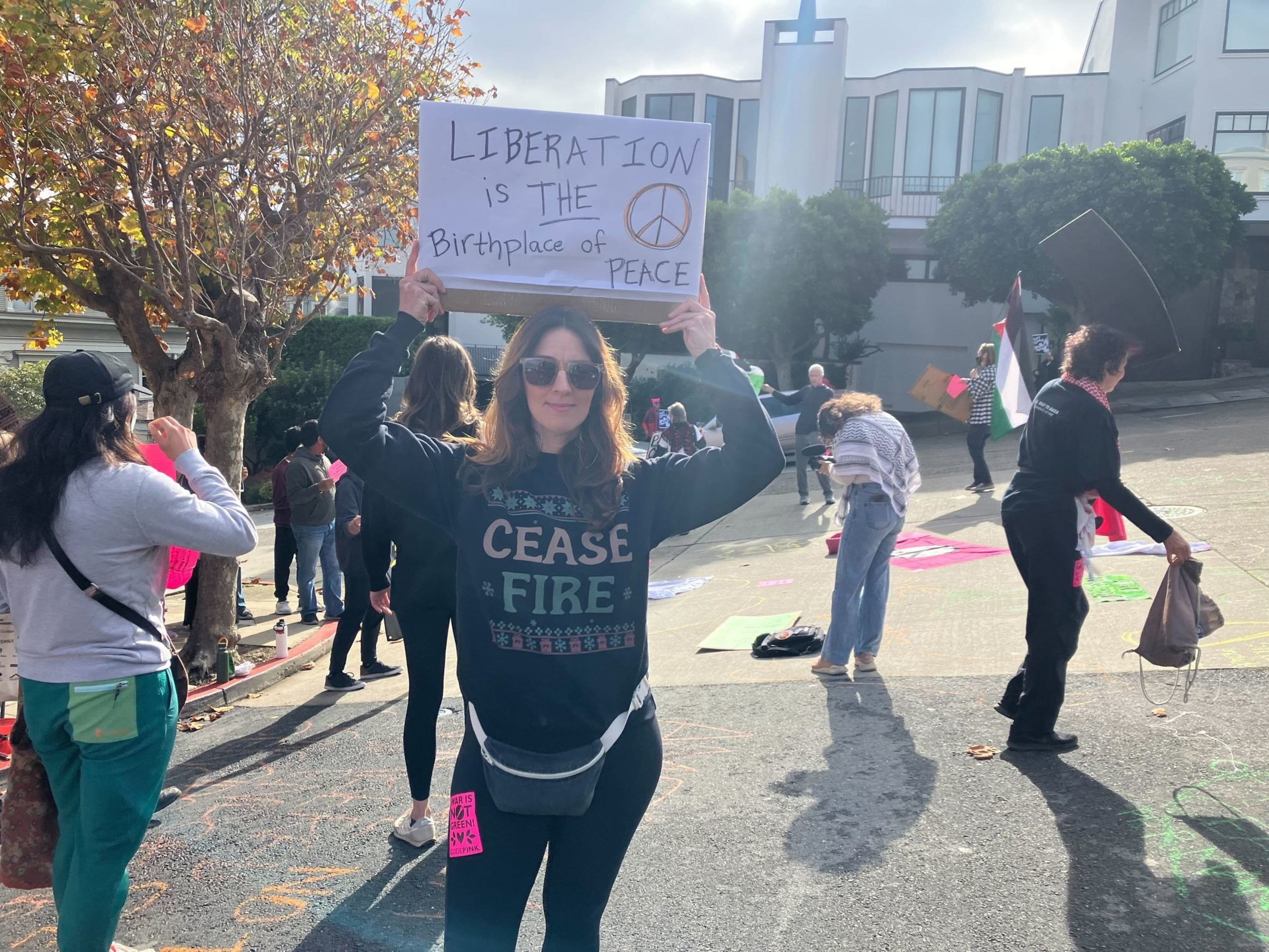 Woman wearing sweatshirt that states cease fire holds sign saying liberation is the birthplace of peace