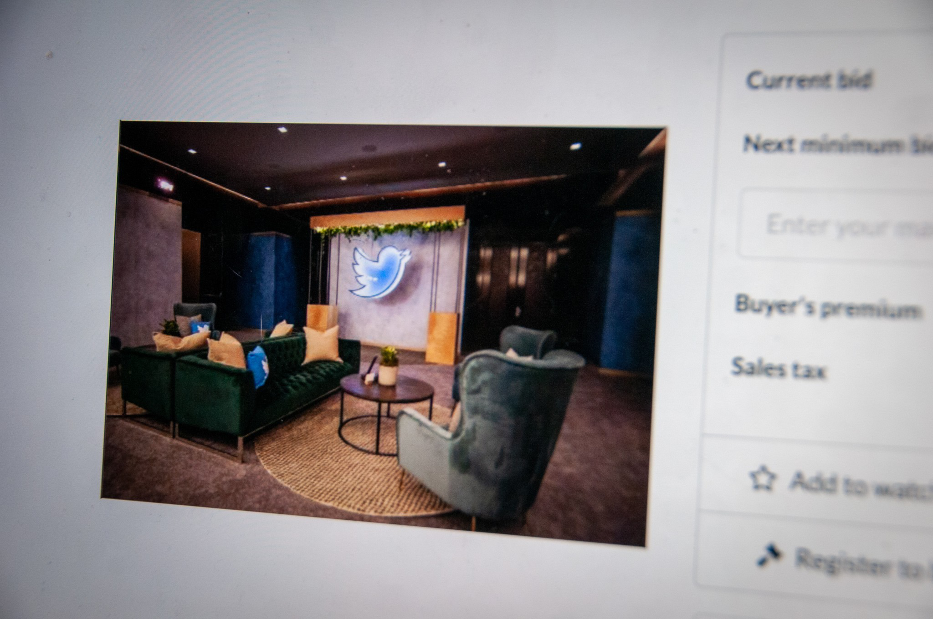A cozy lounge area with green and blue armchairs, yellow pillows, a round rug, and a large illuminated Twitter bird logo on the wall.