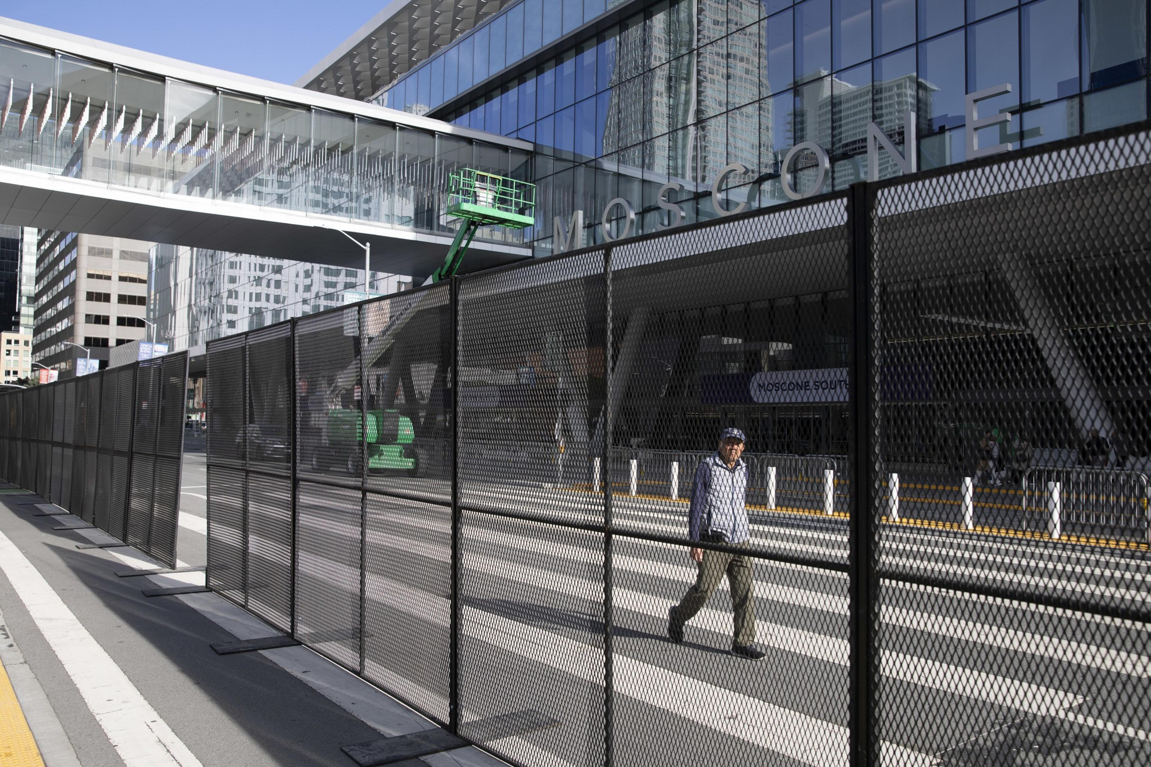 A man walks by a fence in front of the Moscone Center.