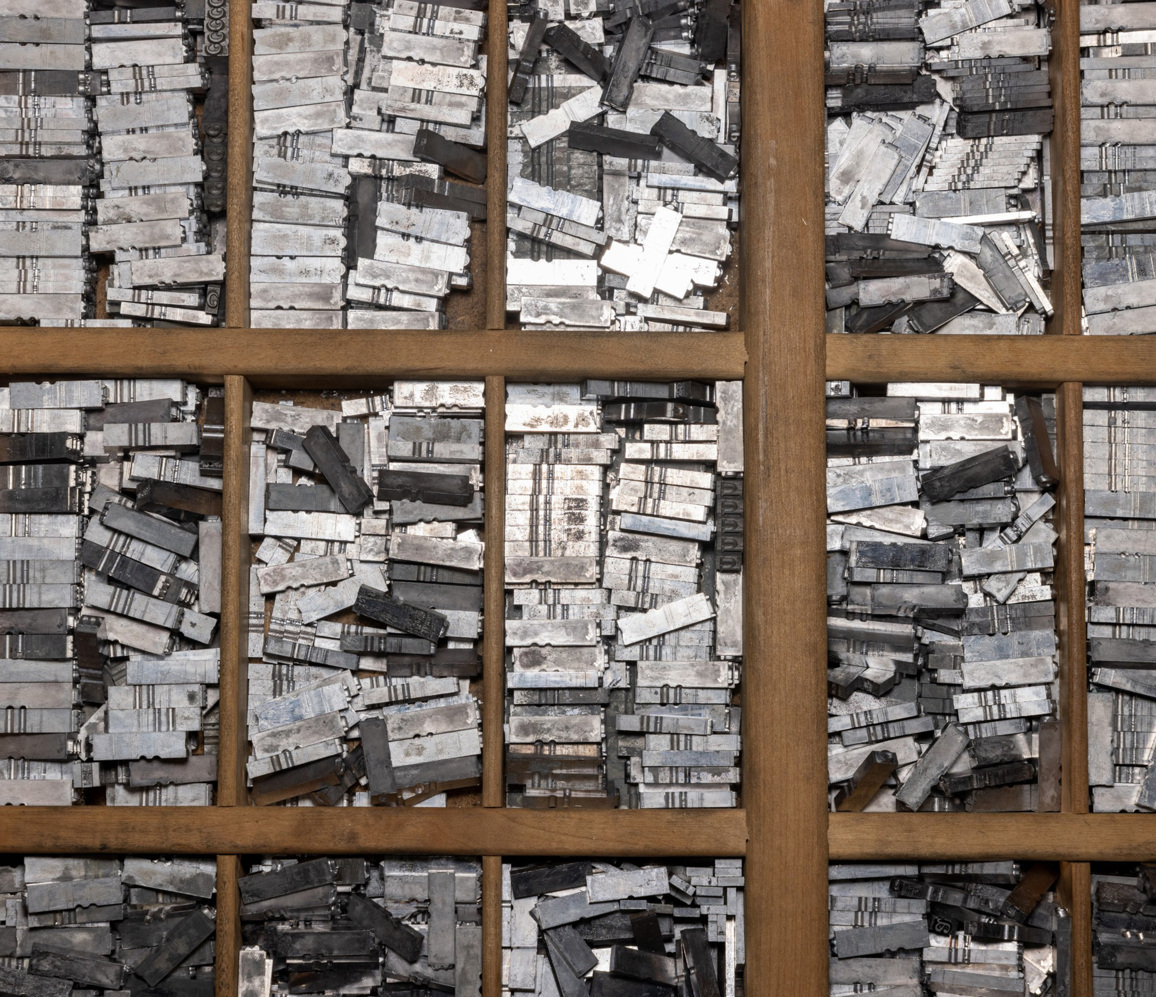 The image shows a pattern of stacked, weathered wooden blocks arranged behind a grid of wooden beams, creating a textured, abstract appearance.