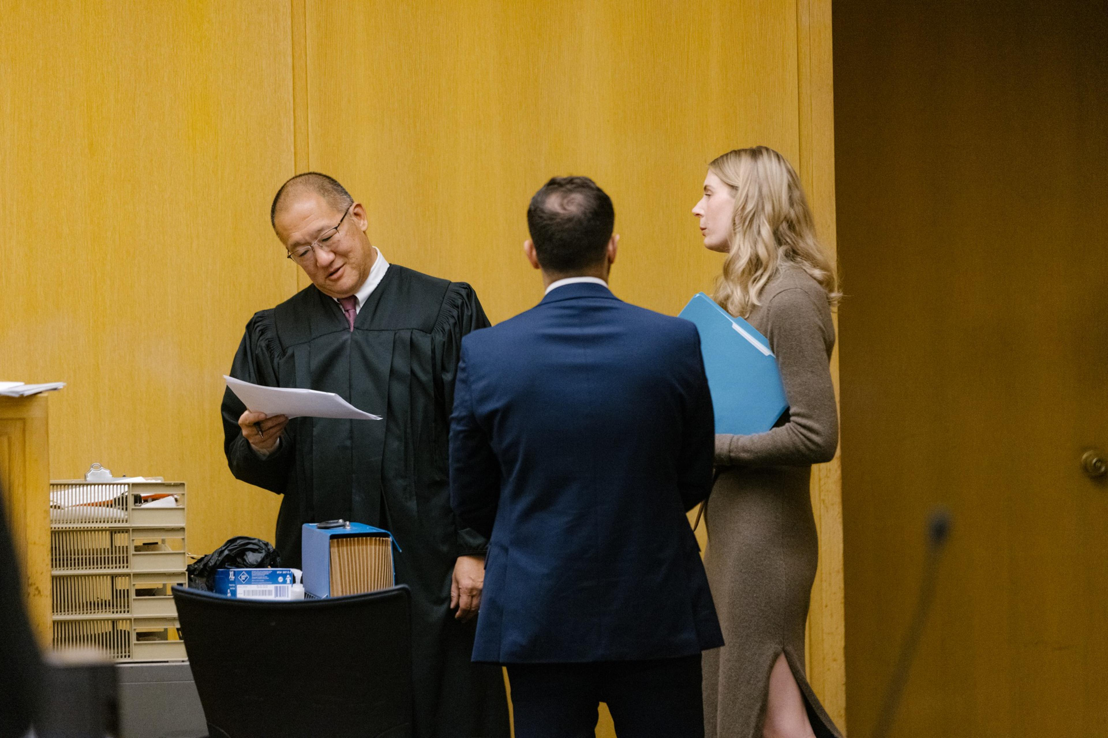 Three people stand in court talking. 