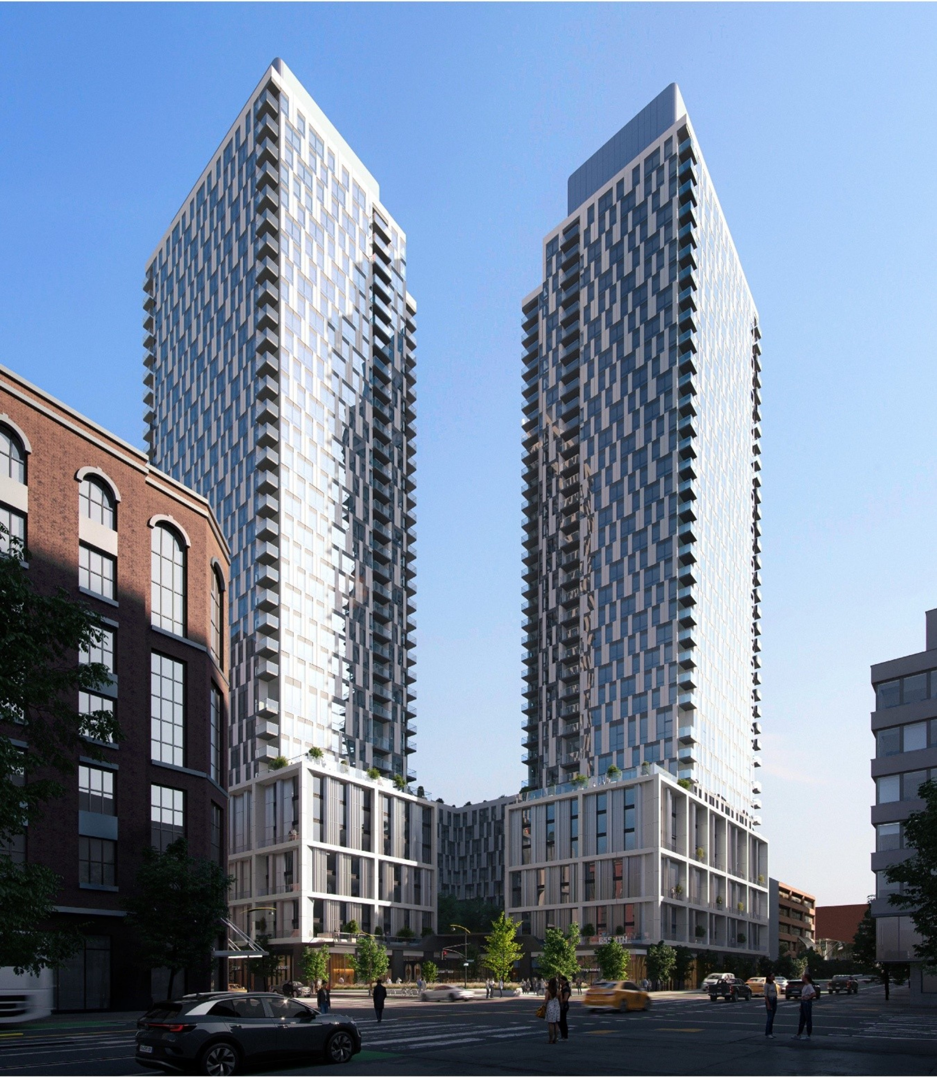 Two tall buildings rise from a shared podium base against a blue sky backdrop next to a city intersection.