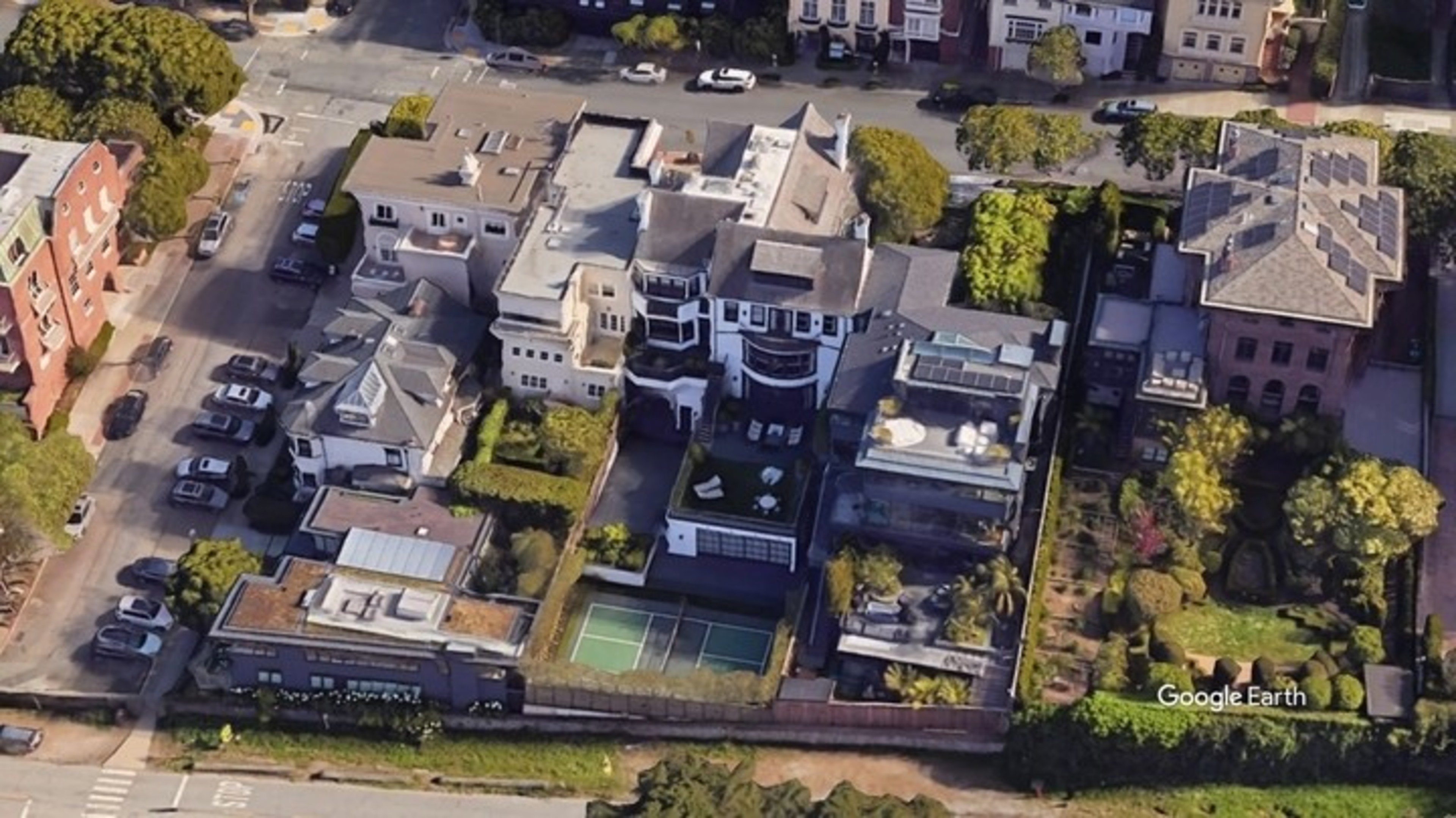 Aerial view of urban buildings with a tennis court, green spaces, and cars on the street, marked by "Google Earth" at the bottom right.