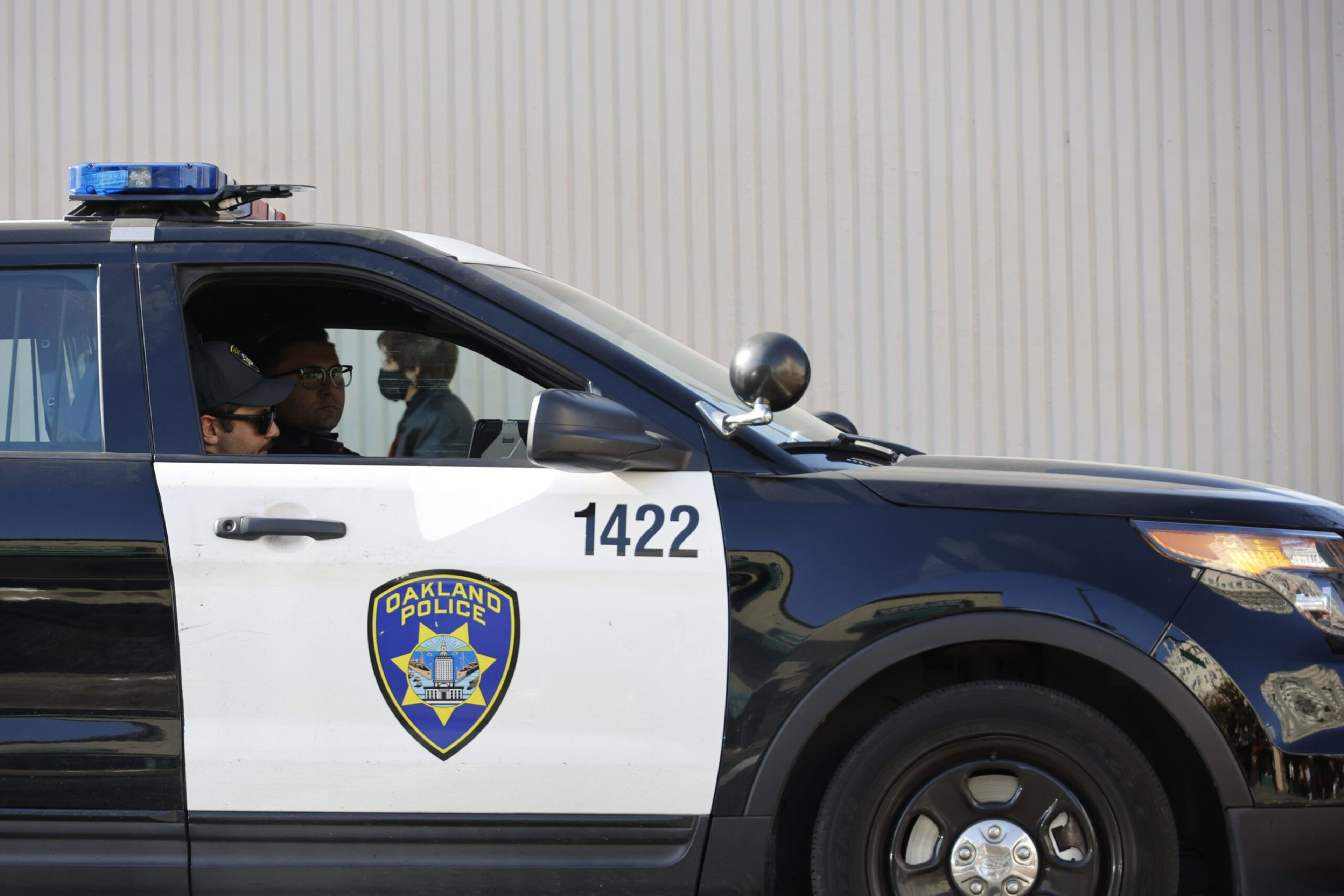 A police officer sits inside a marked Oakland Police vehicle, with badge visible on the car door.