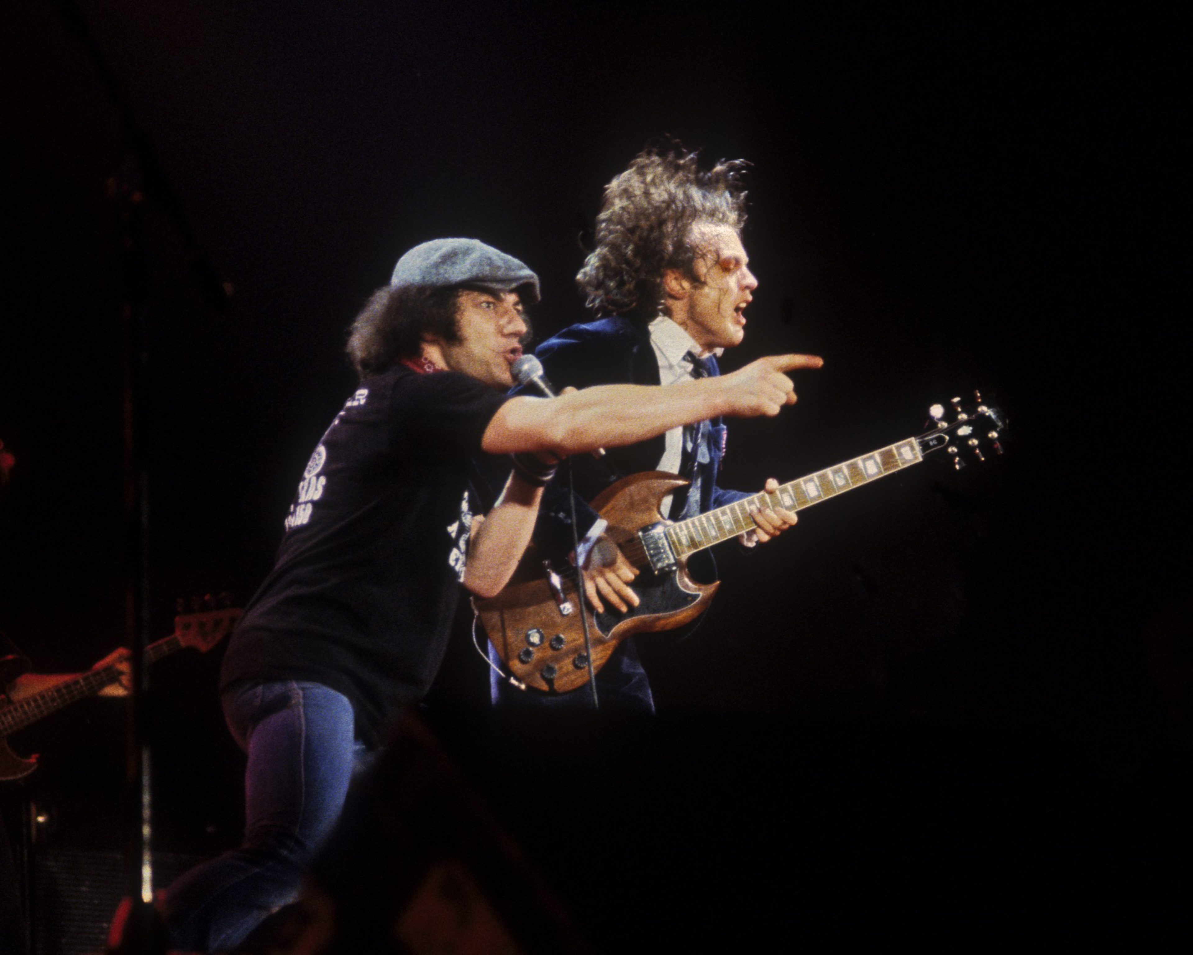 Two musicians on stage. One sings into a mic, the other plays guitar, both animated and passionate in performance.