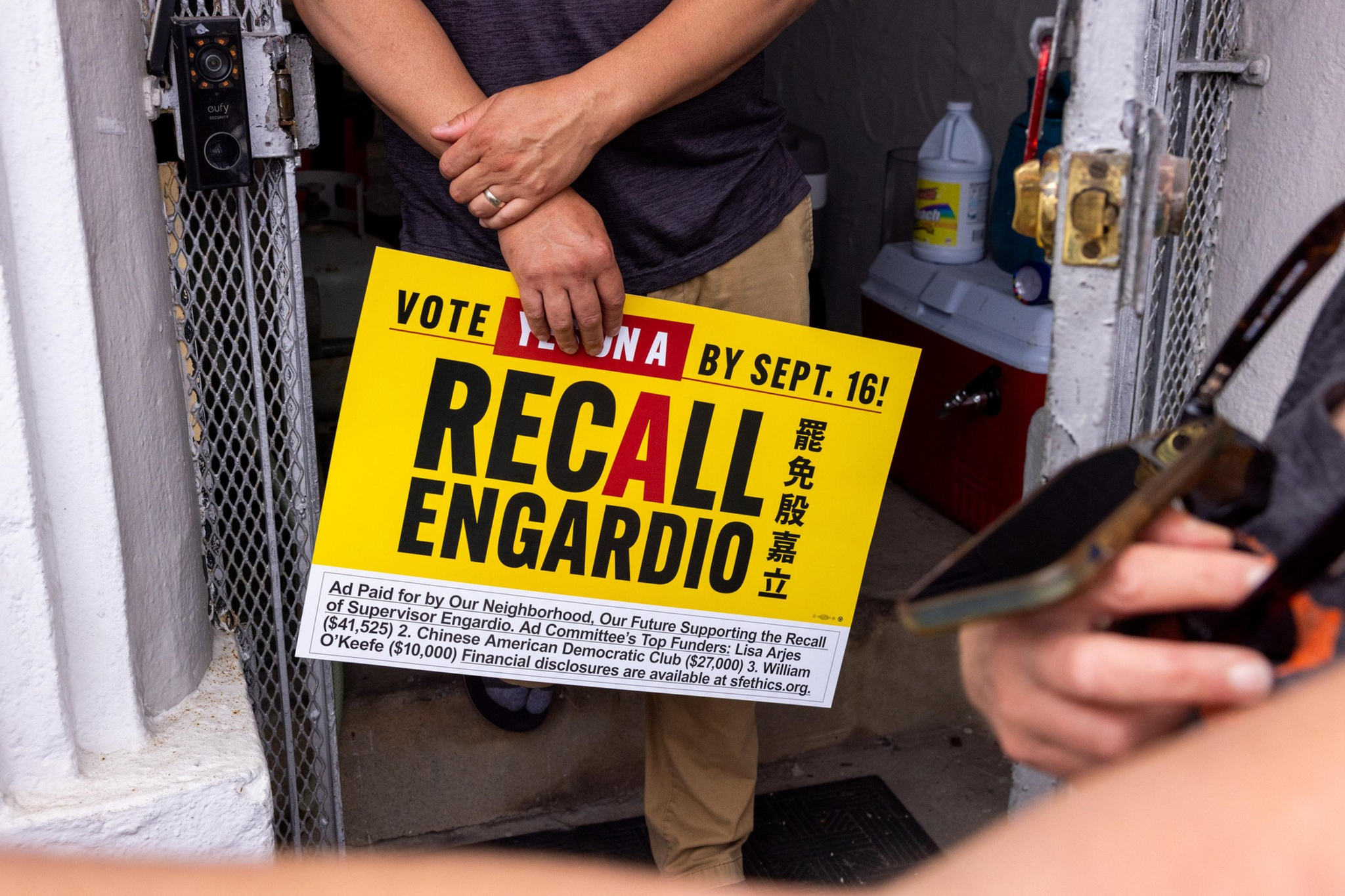 A person holds a yellow sign urging to vote "No" on a recall of Supervisor Engardio by September 16.