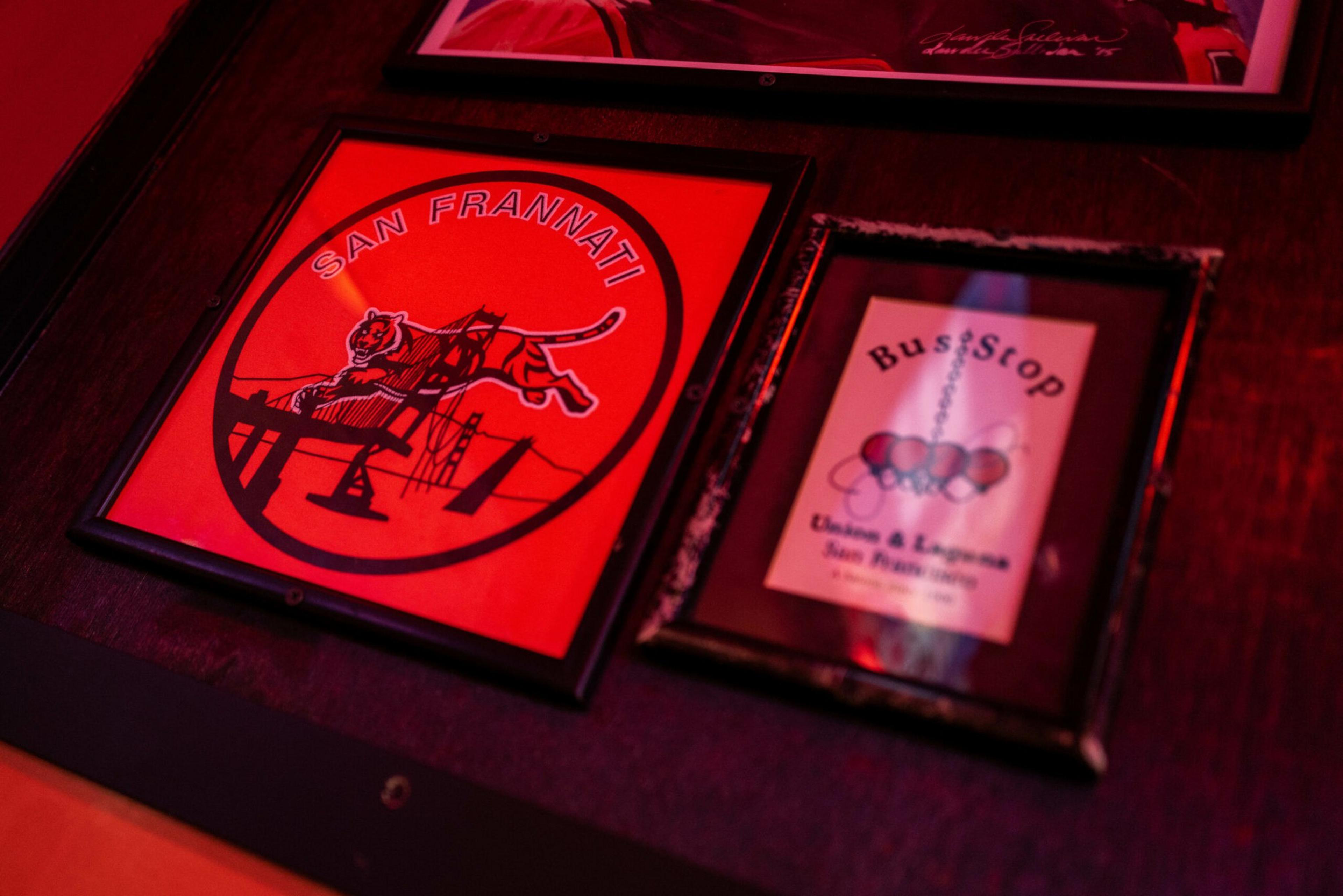 A red and black framed poster with a leaping tiger and "San Frannati" text sits next to a smaller framed card advertising "Bus Stop" cheesesteaks and egg sandwiches.