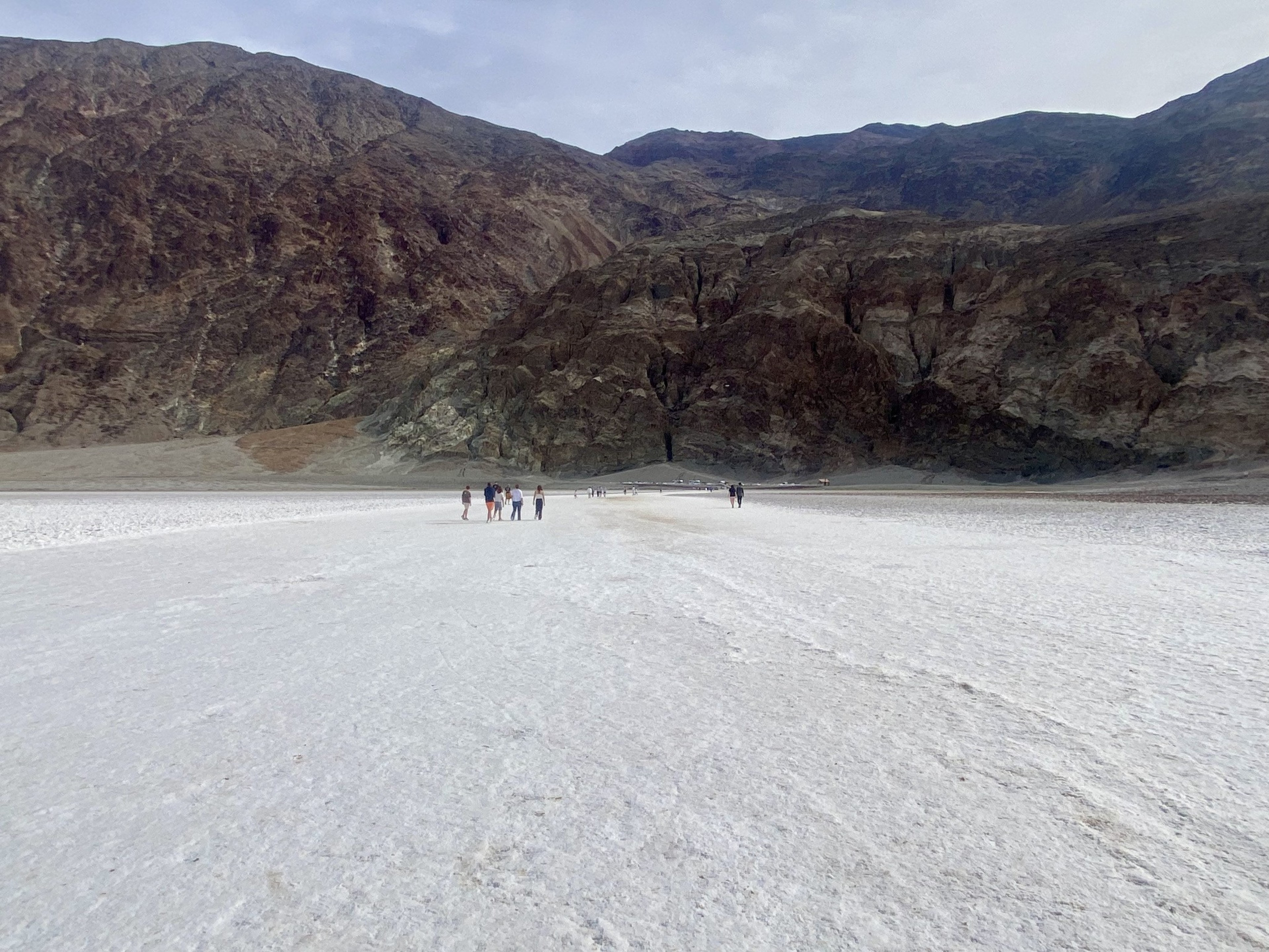 People stand in a desert with white sand in the foreground and craggy mountains in the background.