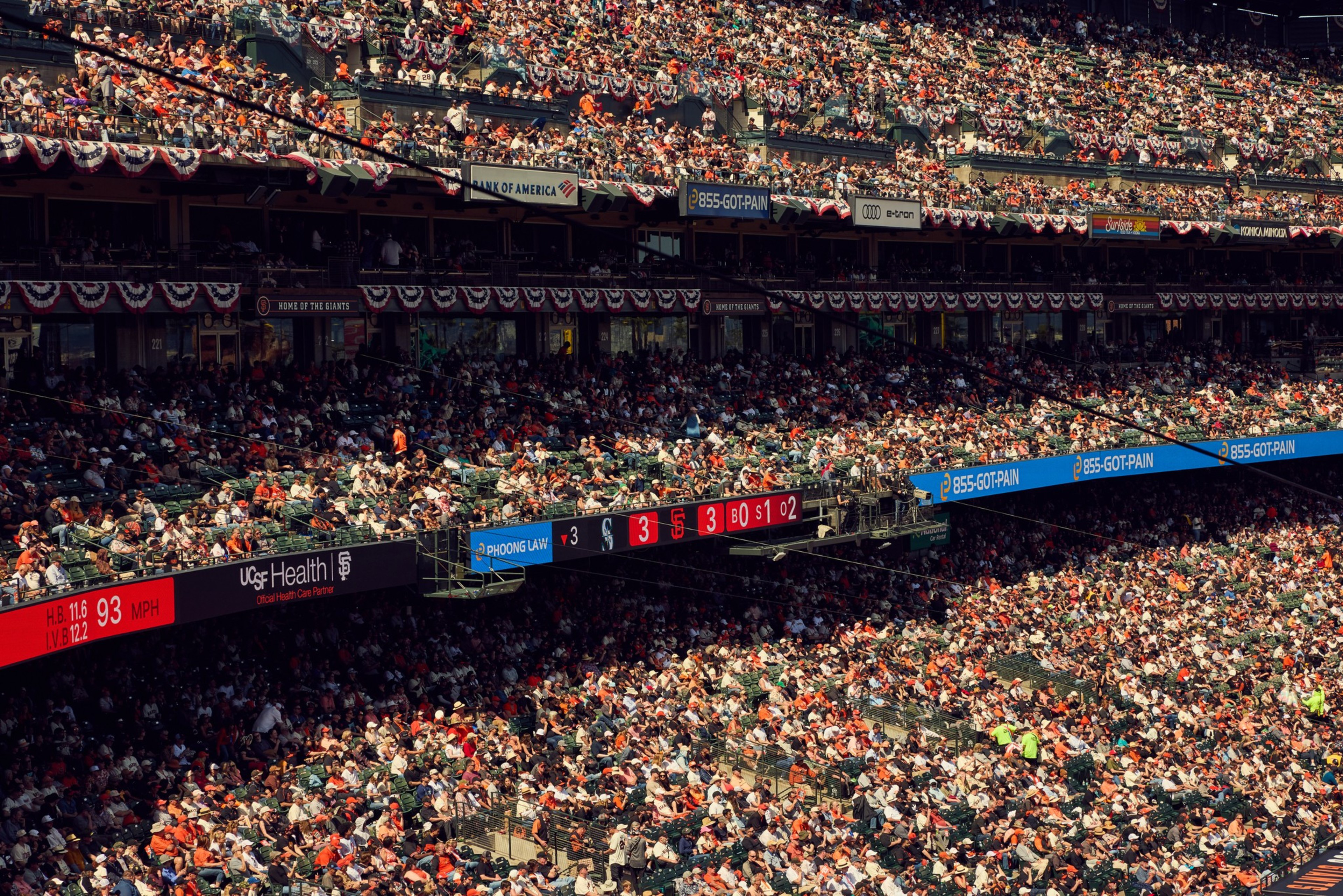 A packed baseball stadium with spectators filling the seats. Banners and ads are visible, along with a scoreboard indicating a tie game at 3-3.
