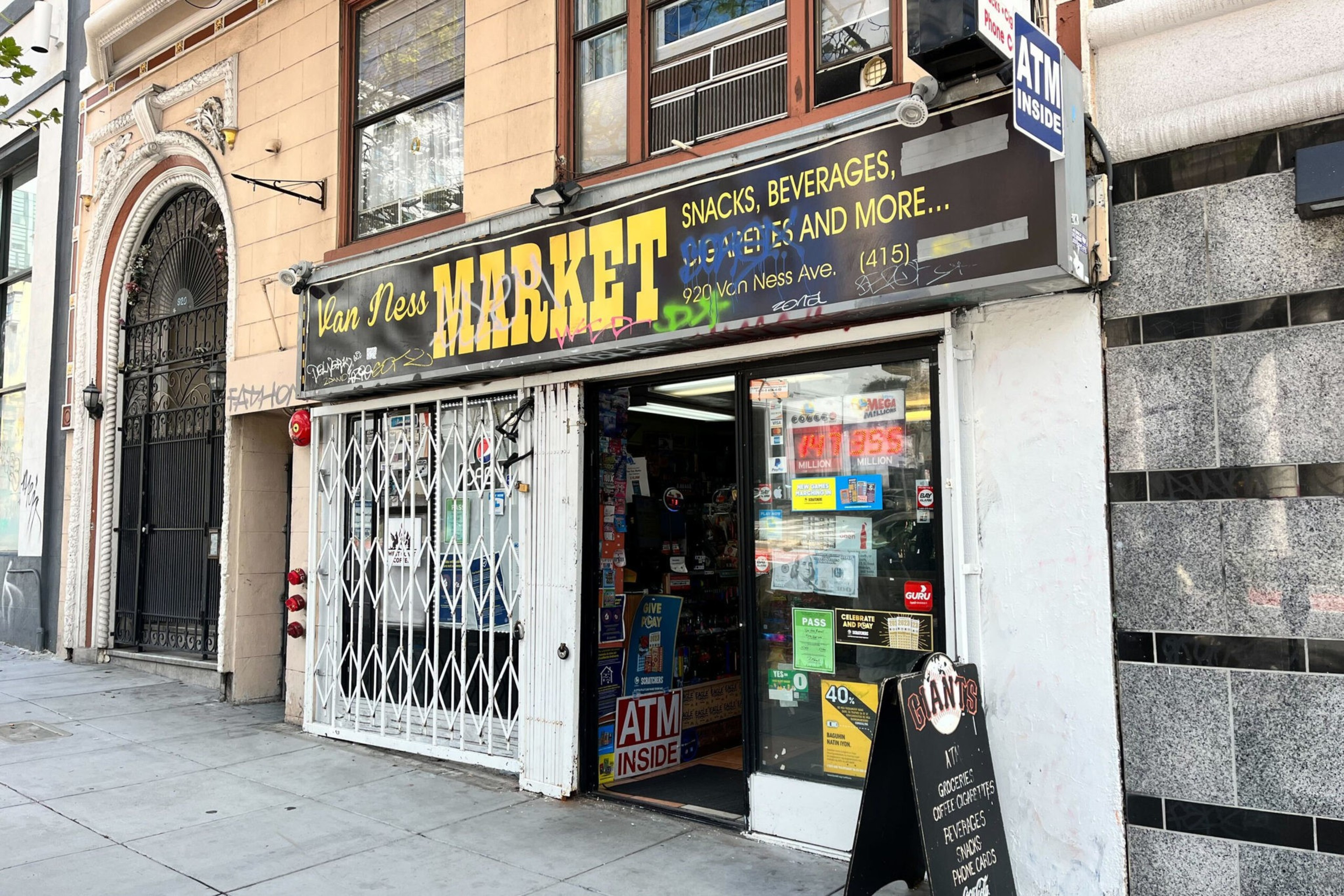 Van Ness Market sells snacks, beverages, groceries, and gift certificates, with an ATM inside and a black sandwich board sign outside.