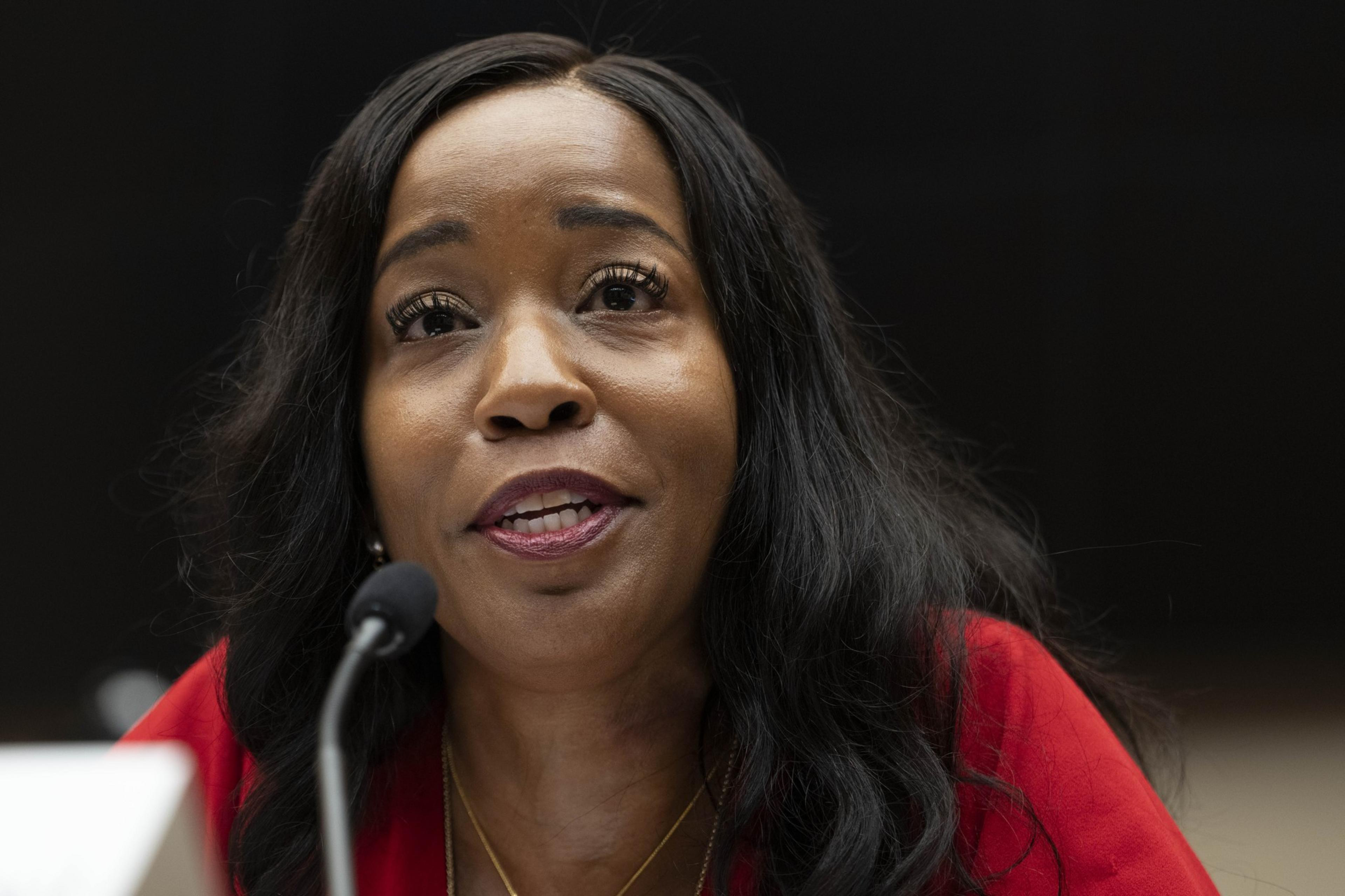 A woman speaking into a microphone, wearing a red top, with a focused and expressive look.