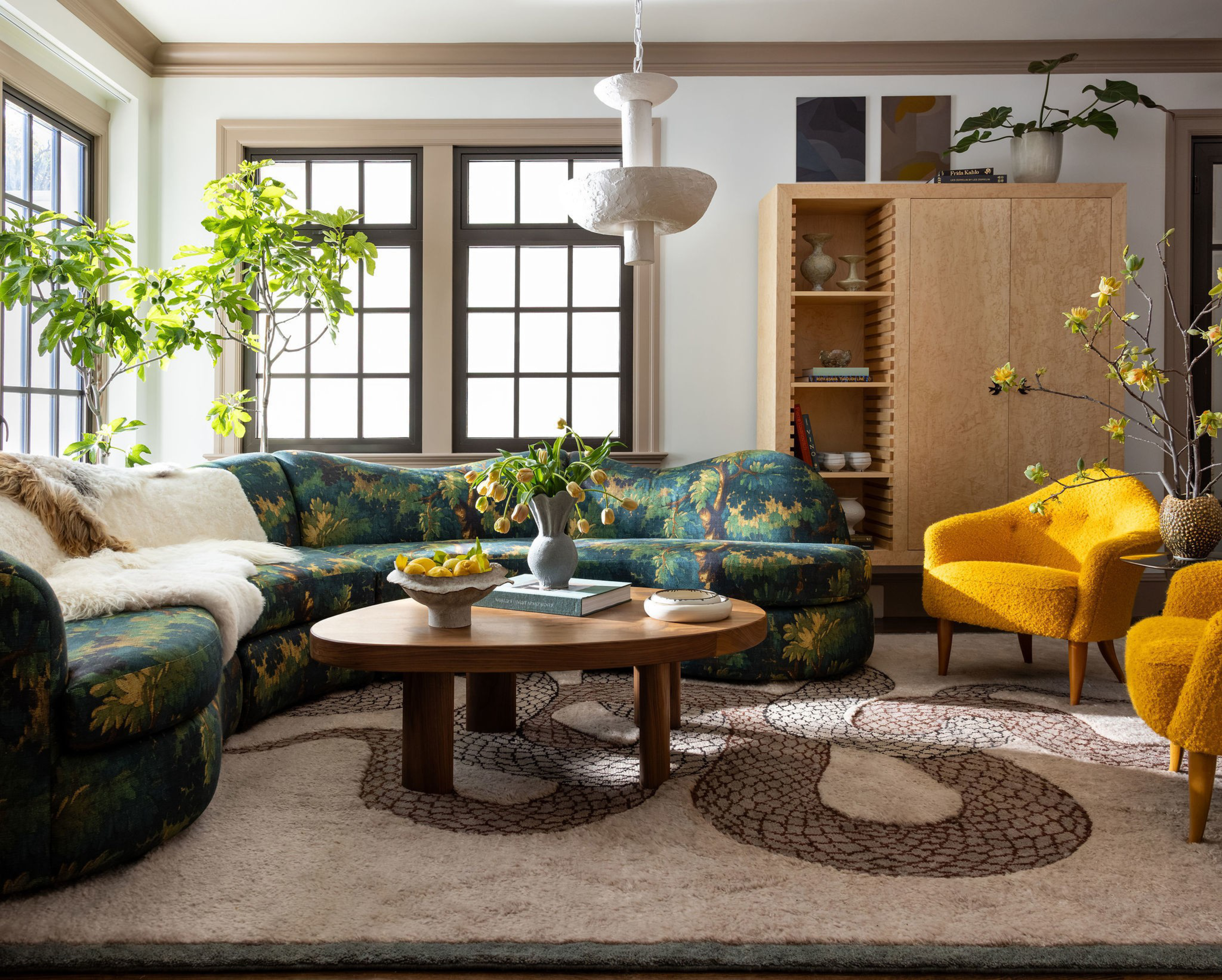 A cozy living room features a floral-patterned sectional sofa, two bright yellow armchairs, a wooden coffee table with decor, and a light rug with abstract designs.