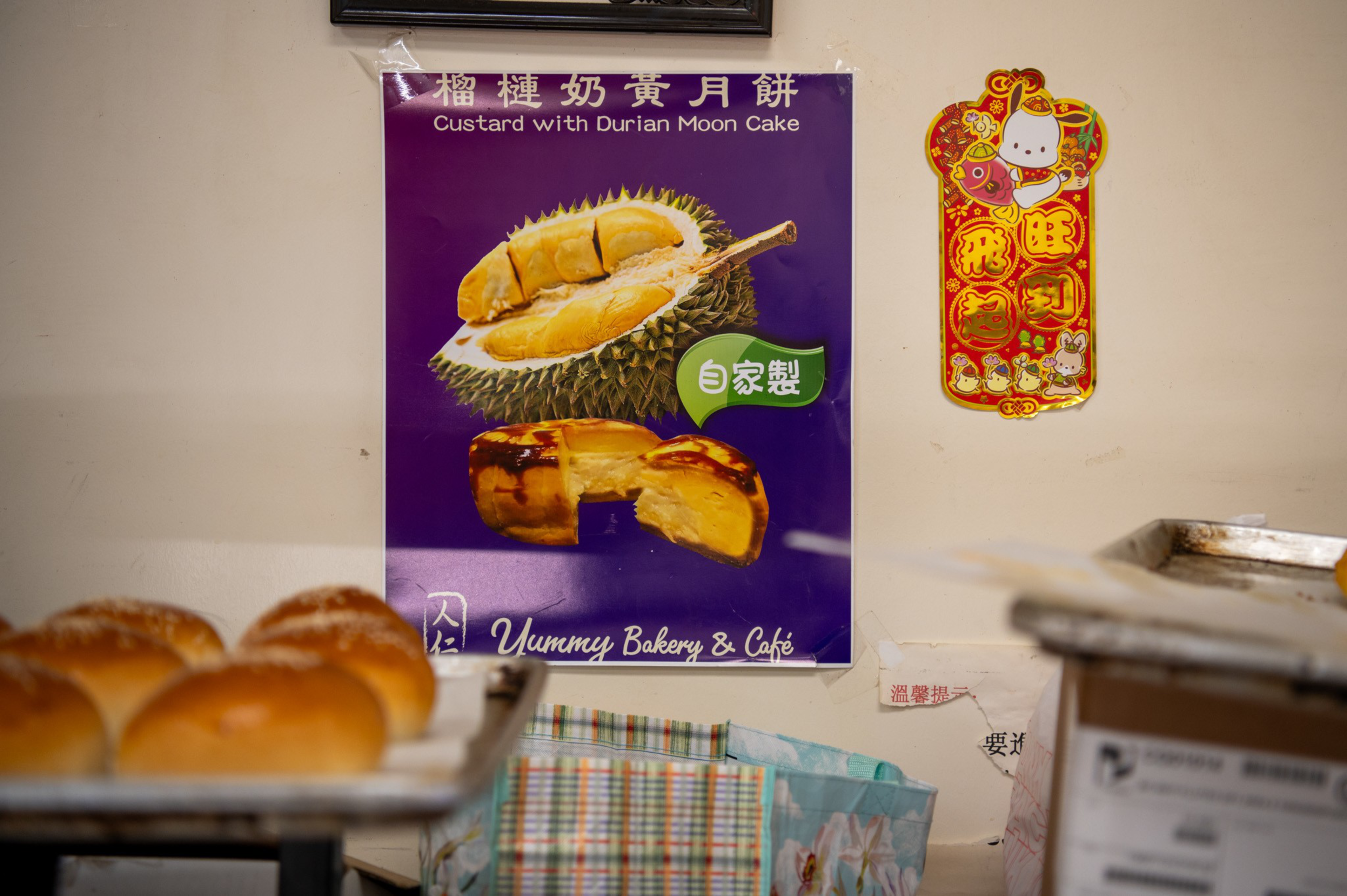 A poster features a custard durian mooncake with an image of a durian fruit and mooncake; nearby are baked bread rolls and colorful boxes.
