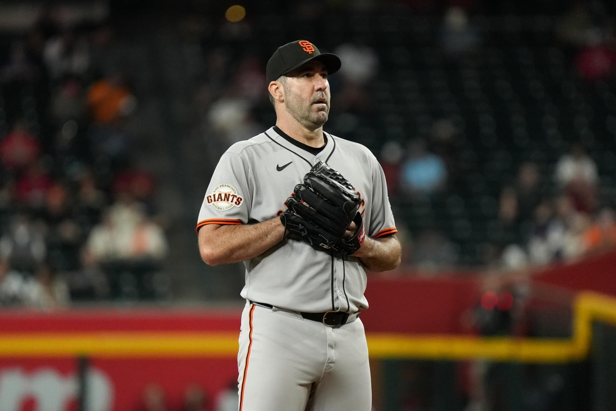 A baseball player in a San Francisco Giants uniform stands on the field, holding a glove, focused and ready to pitch.