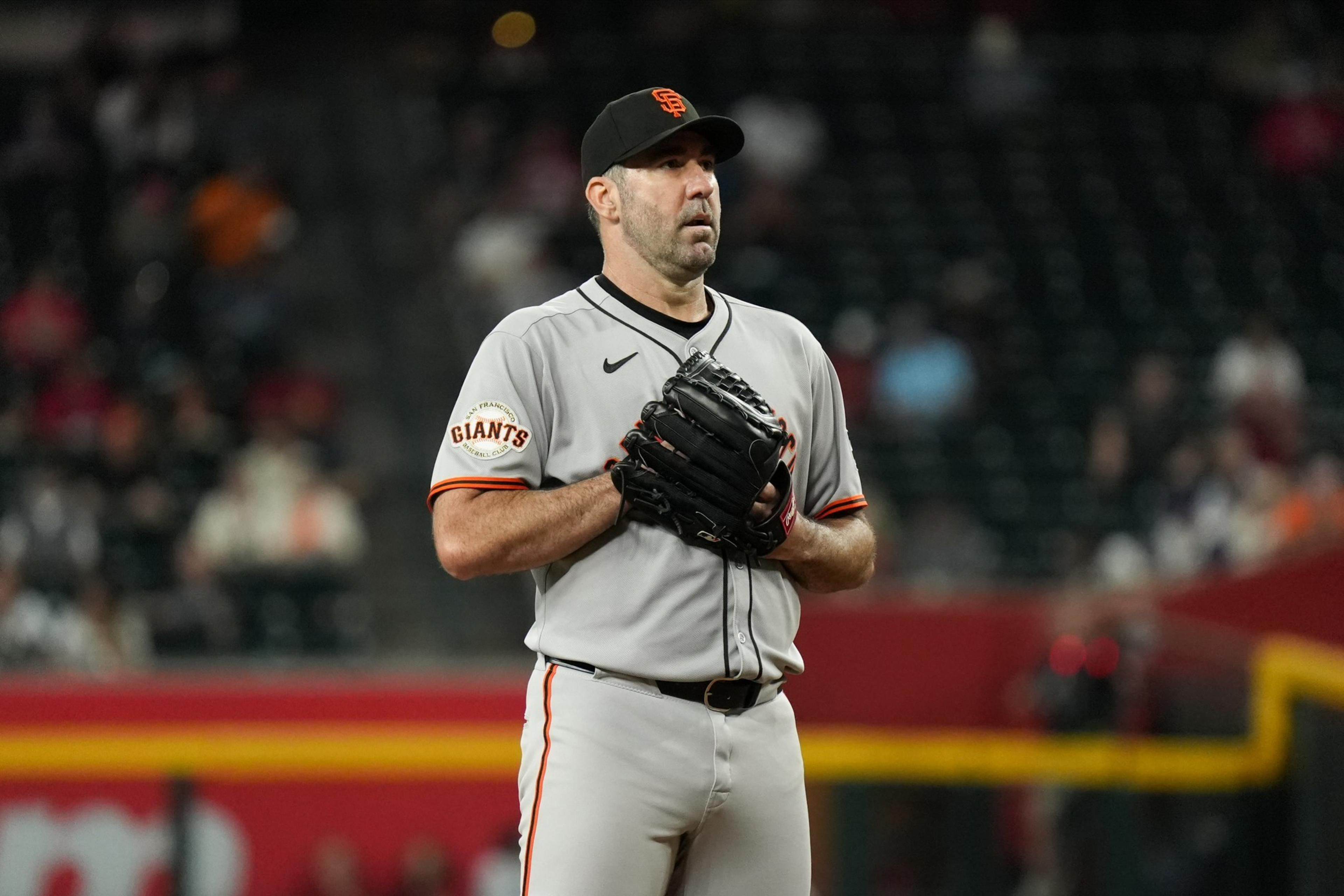 A baseball player in a San Francisco Giants uniform stands on the field, holding a glove, focused and ready to pitch.