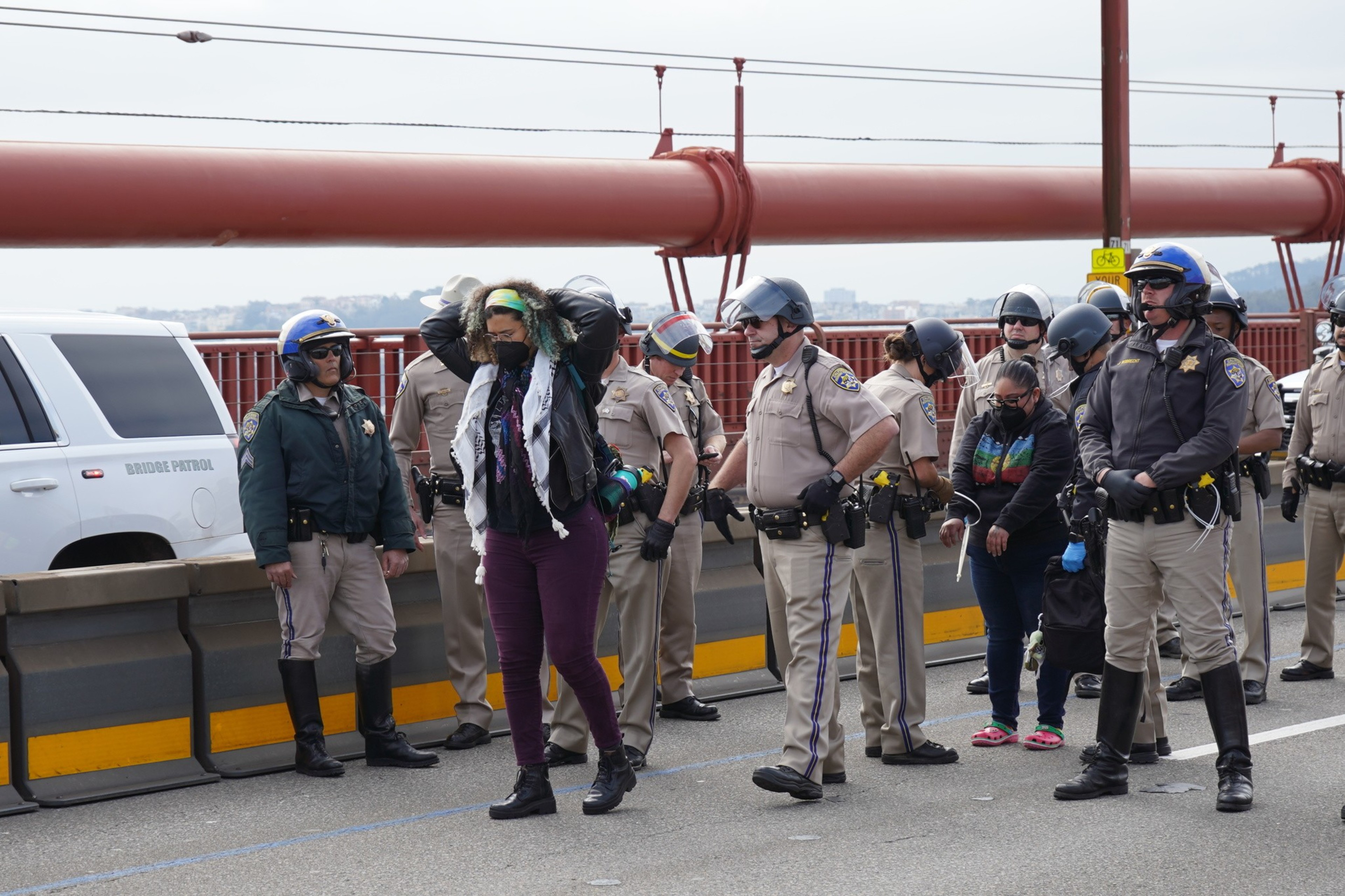 Law enforcement officers detain a person on a bridge with a patrol vehicle nearby.