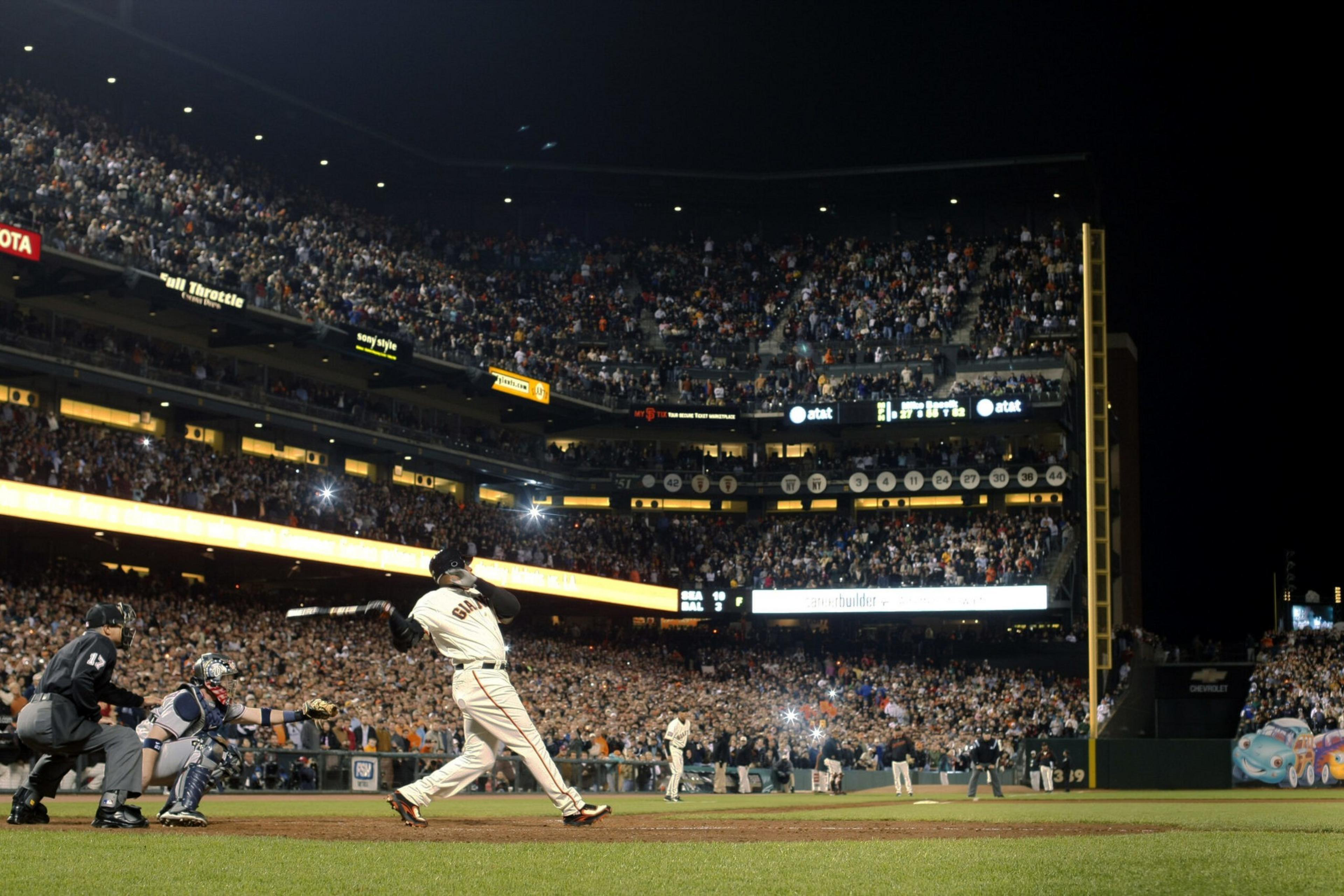A baseball player in a Giants uniform swings at a pitch during a night game with a large crowd watching in the stadium.