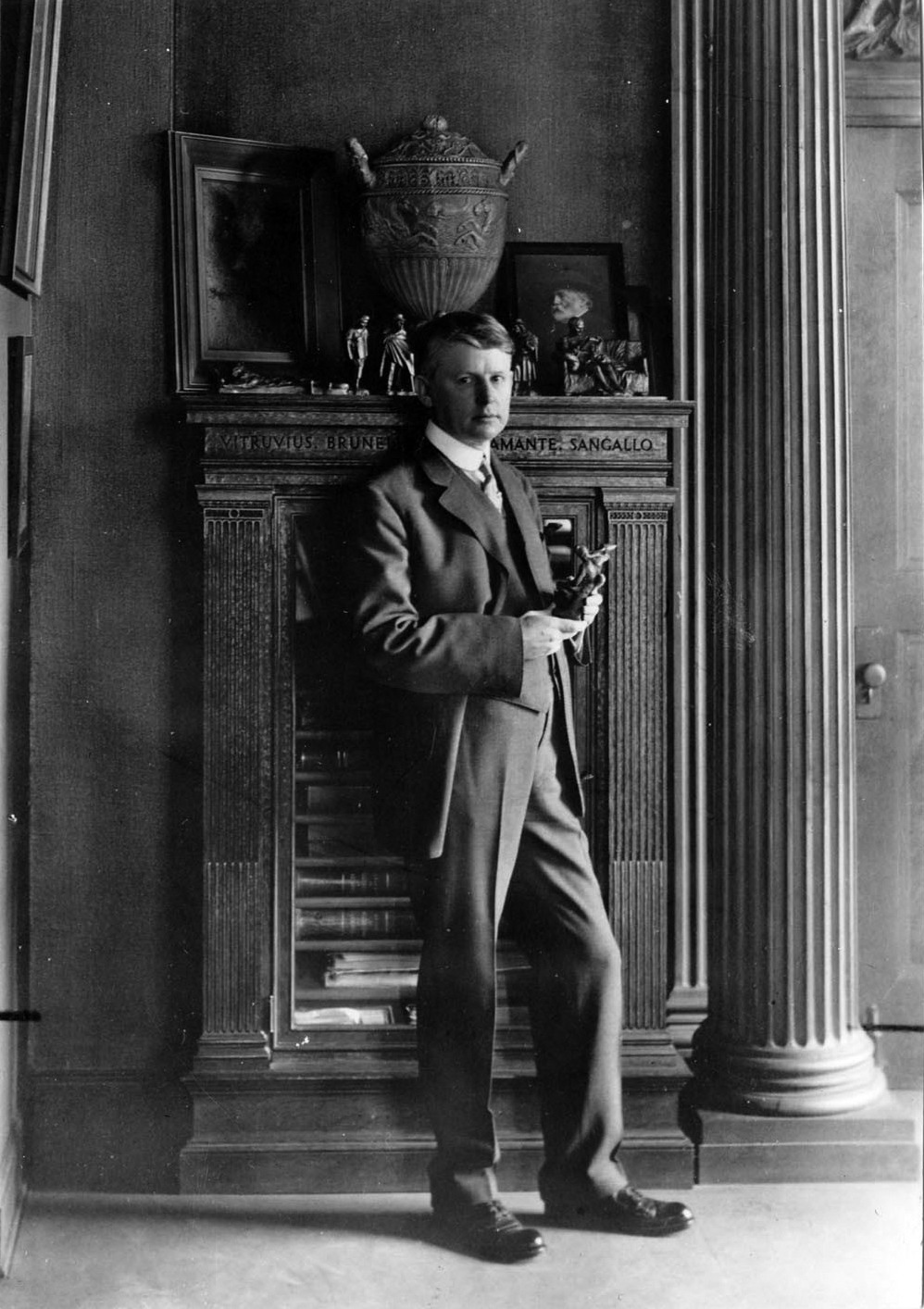 A man stands in front of a piece of furniture holding a statue.