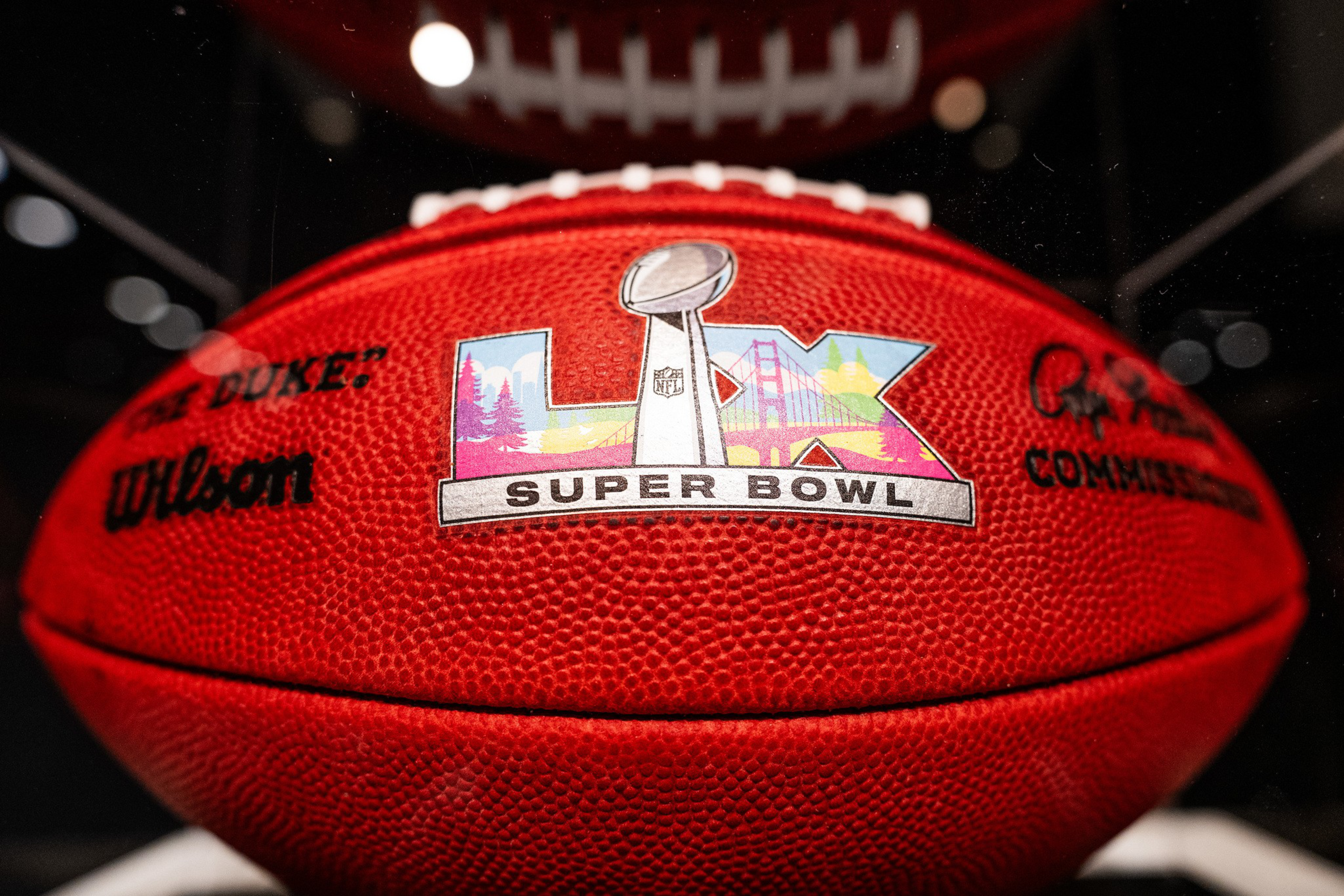 A red NFL football with a “LIX Super Bowl” logo featuring a Lombardi trophy, Golden Gate Bridge, and colorful scenic design is prominently displayed.