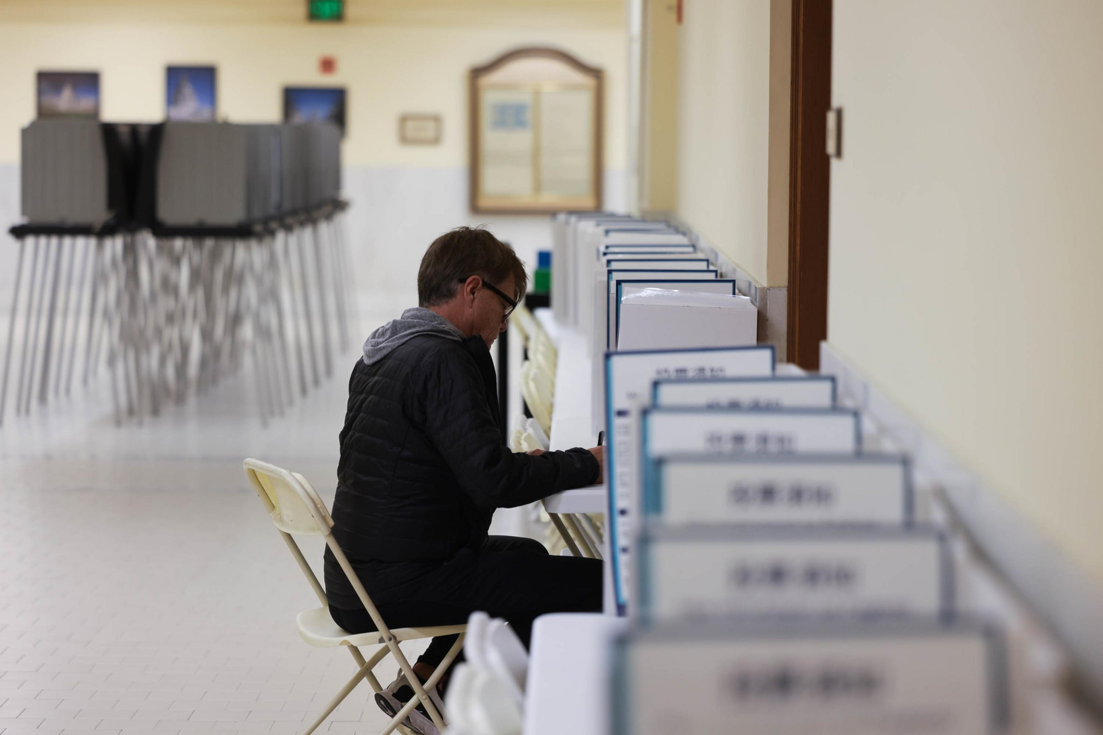 A person is seated at a row of voting booths in a well-lit room, filling out a ballot.