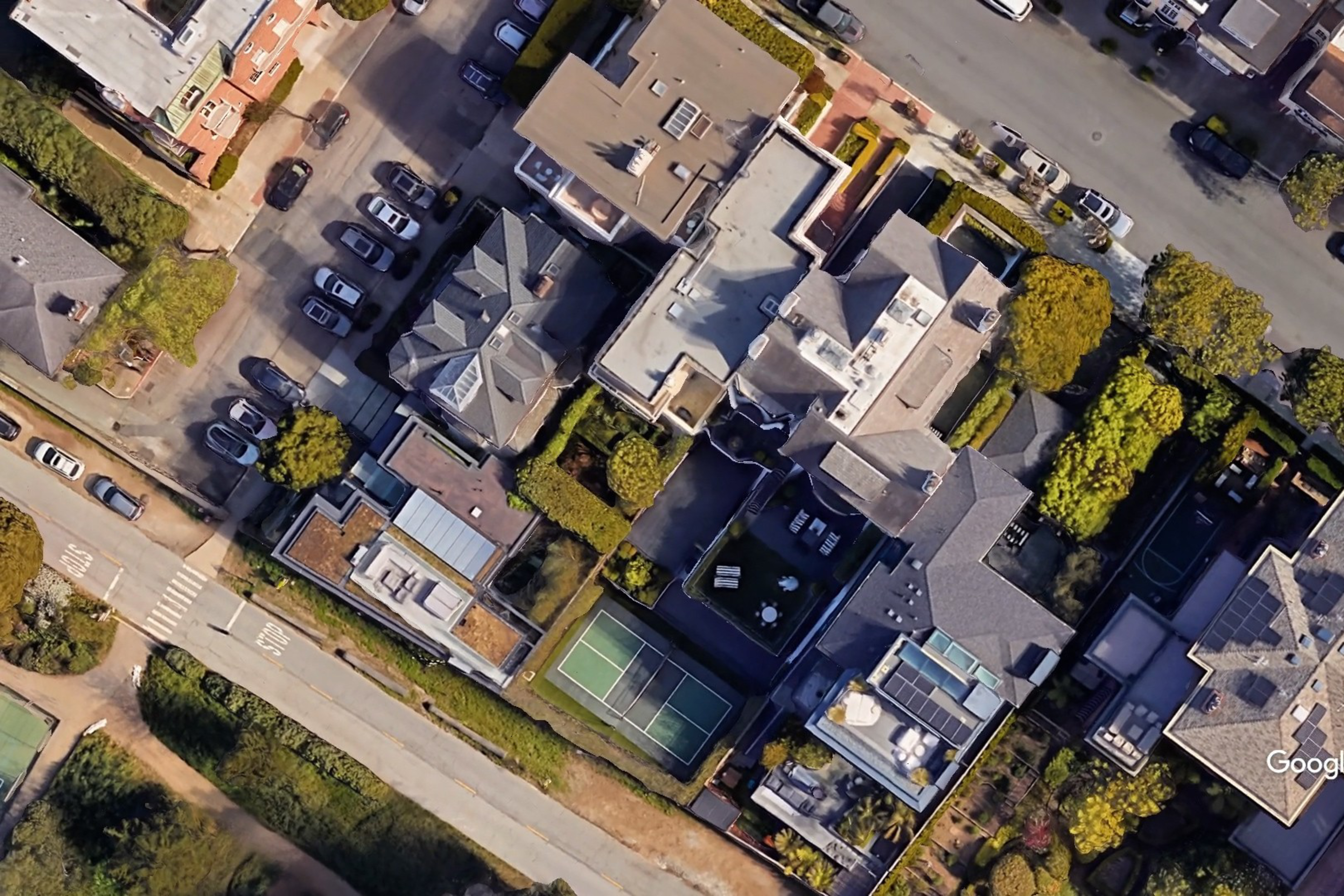Aerial view of a neighborhood with houses, trees, cars and a tennis court.